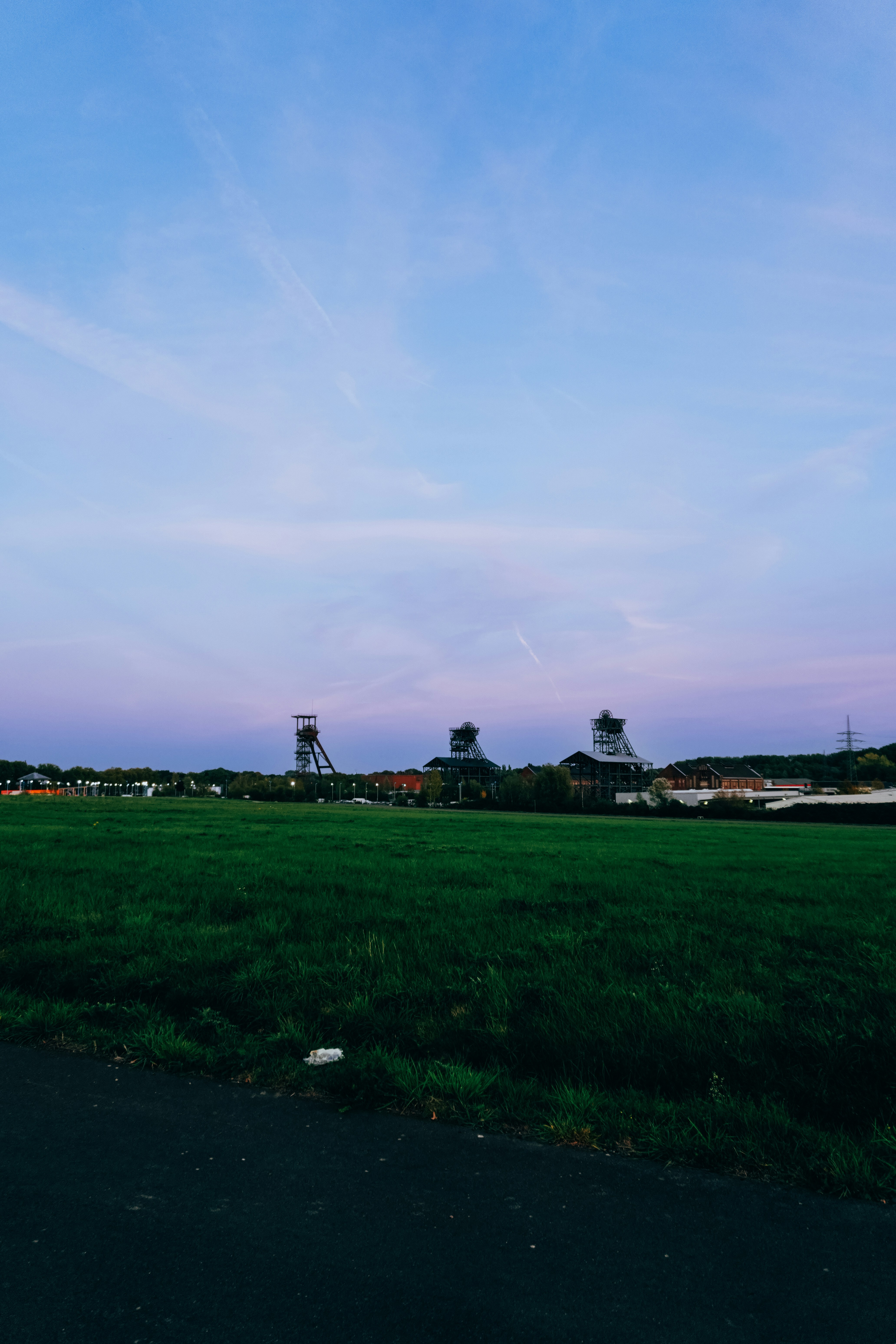 Three industrial headframes rising above a green field under a soft purple and blue sky