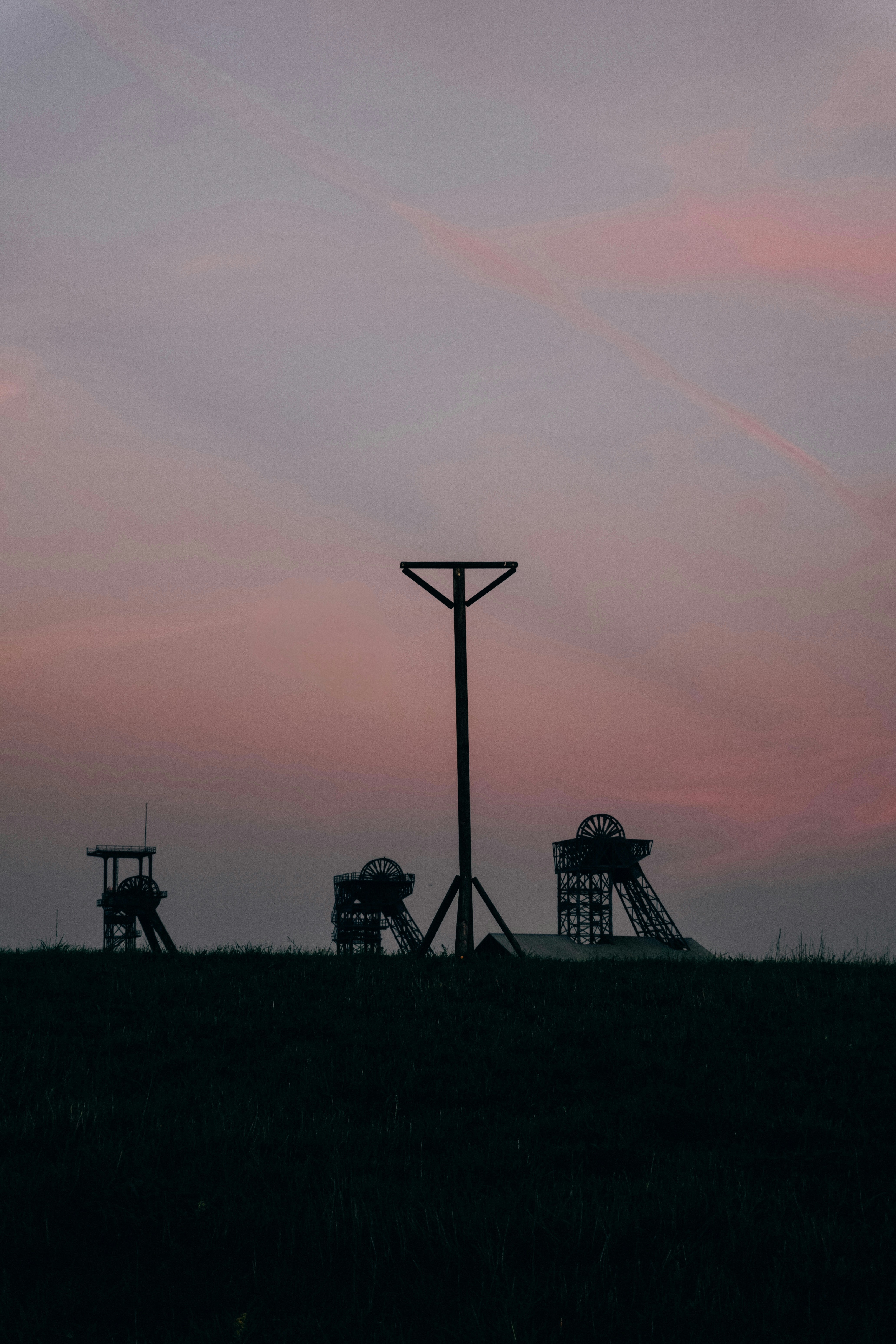 Silhouettes of industrial mine headframes against a soft pink and purple sky