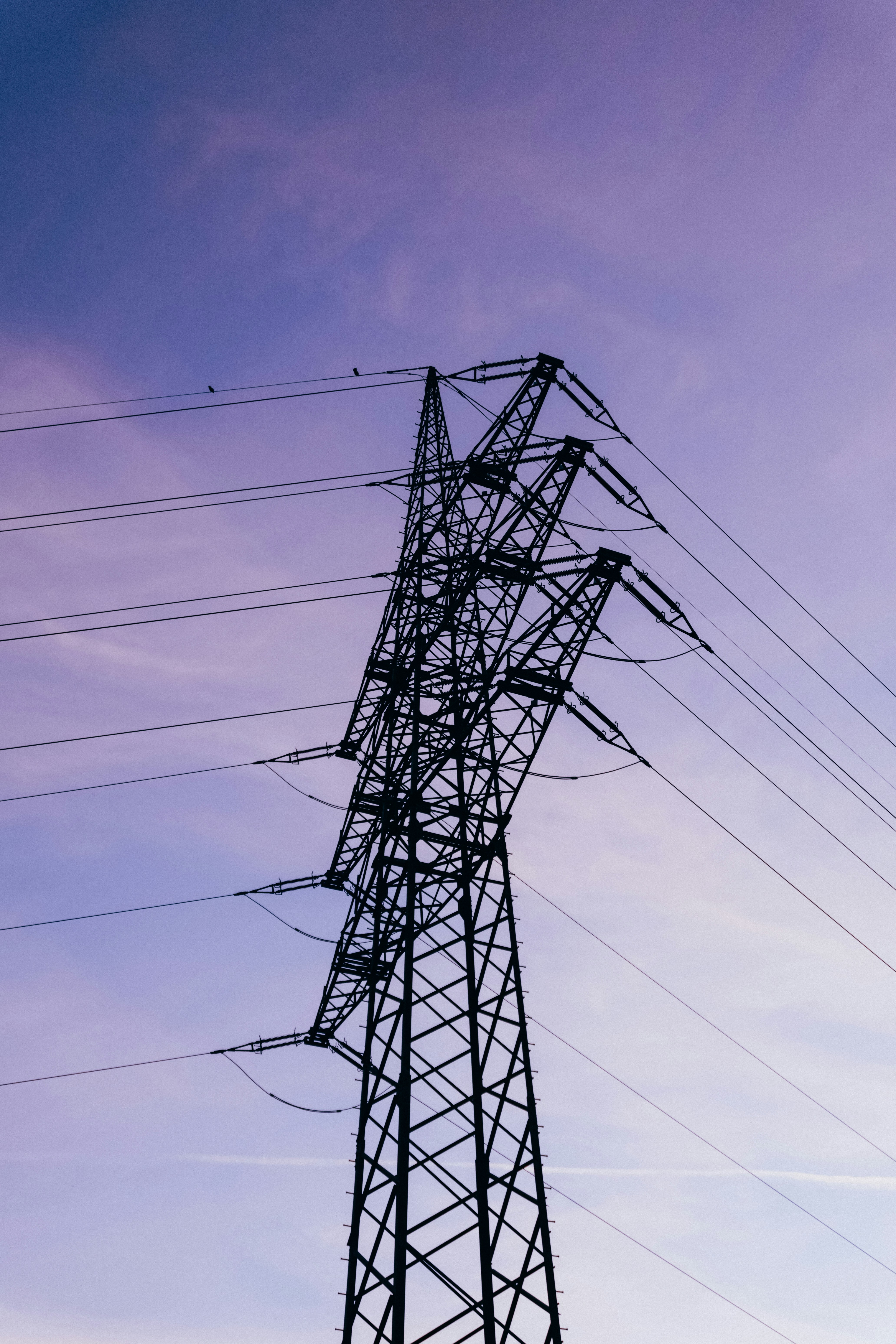 A silhouette of a tall electricity pylon against a soft purple sky