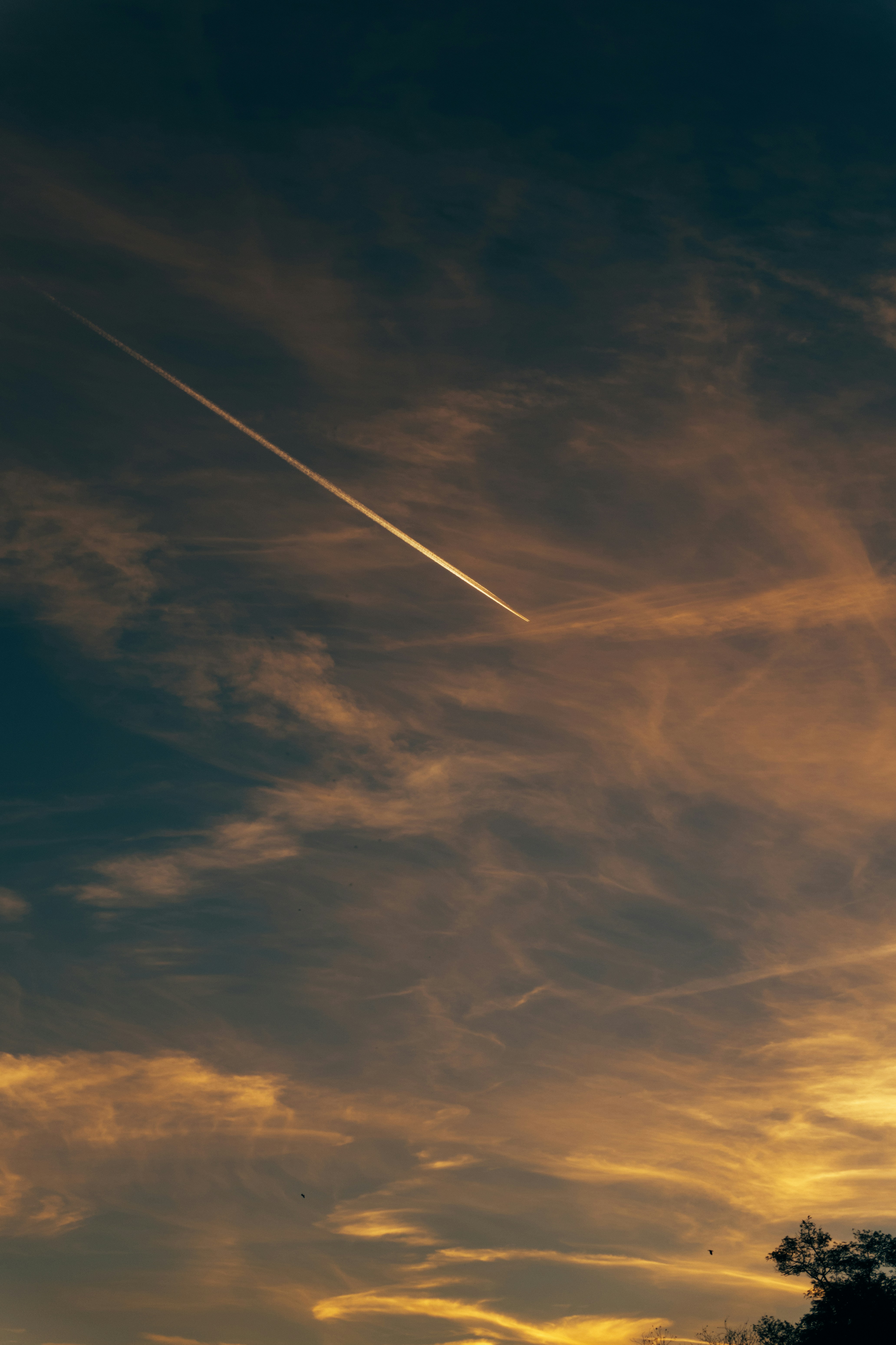 A long airplane contrail cutting across a warm orange and blue sky
