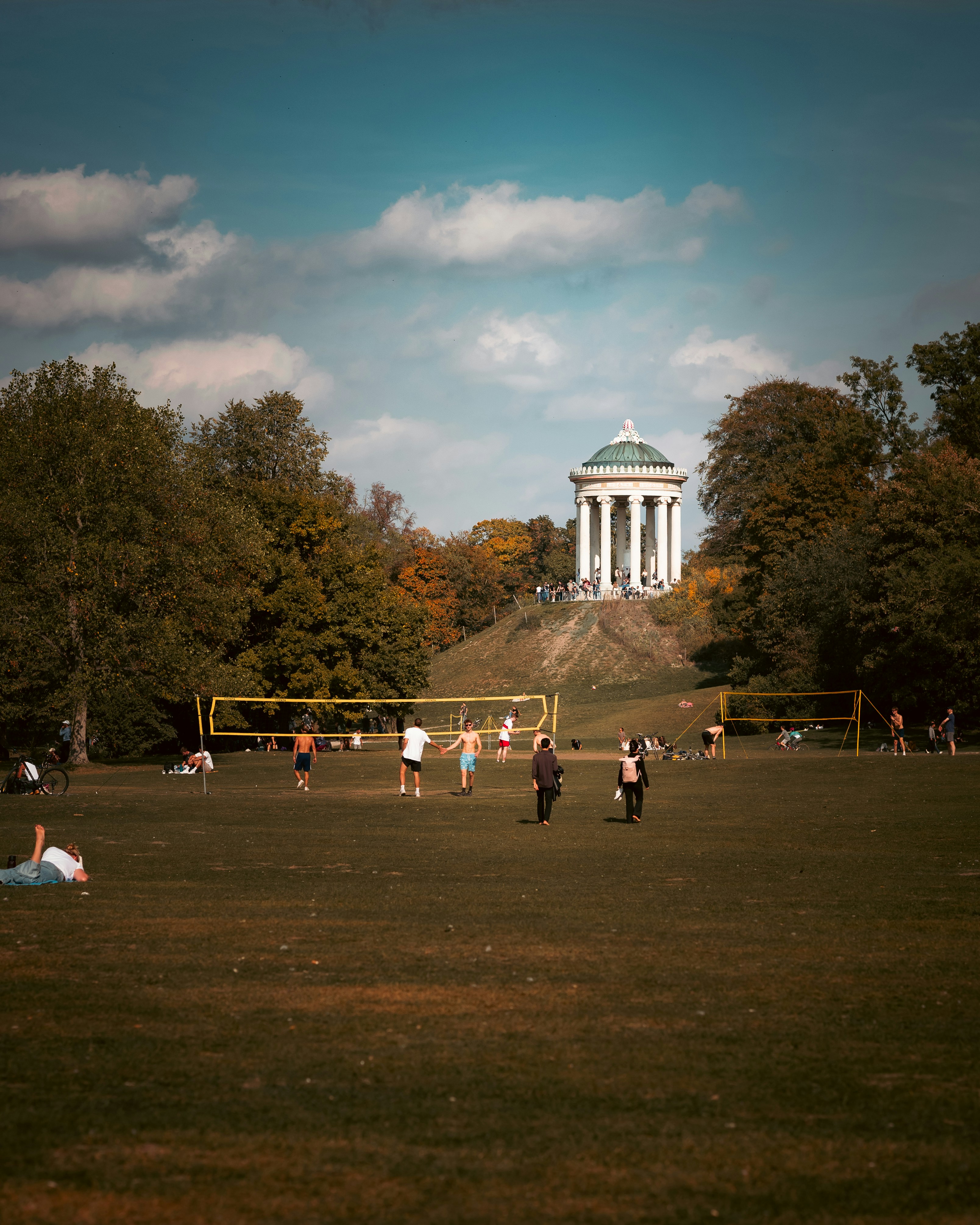 People playing volleyball on a grassy field near the Monopteros temple in Munich