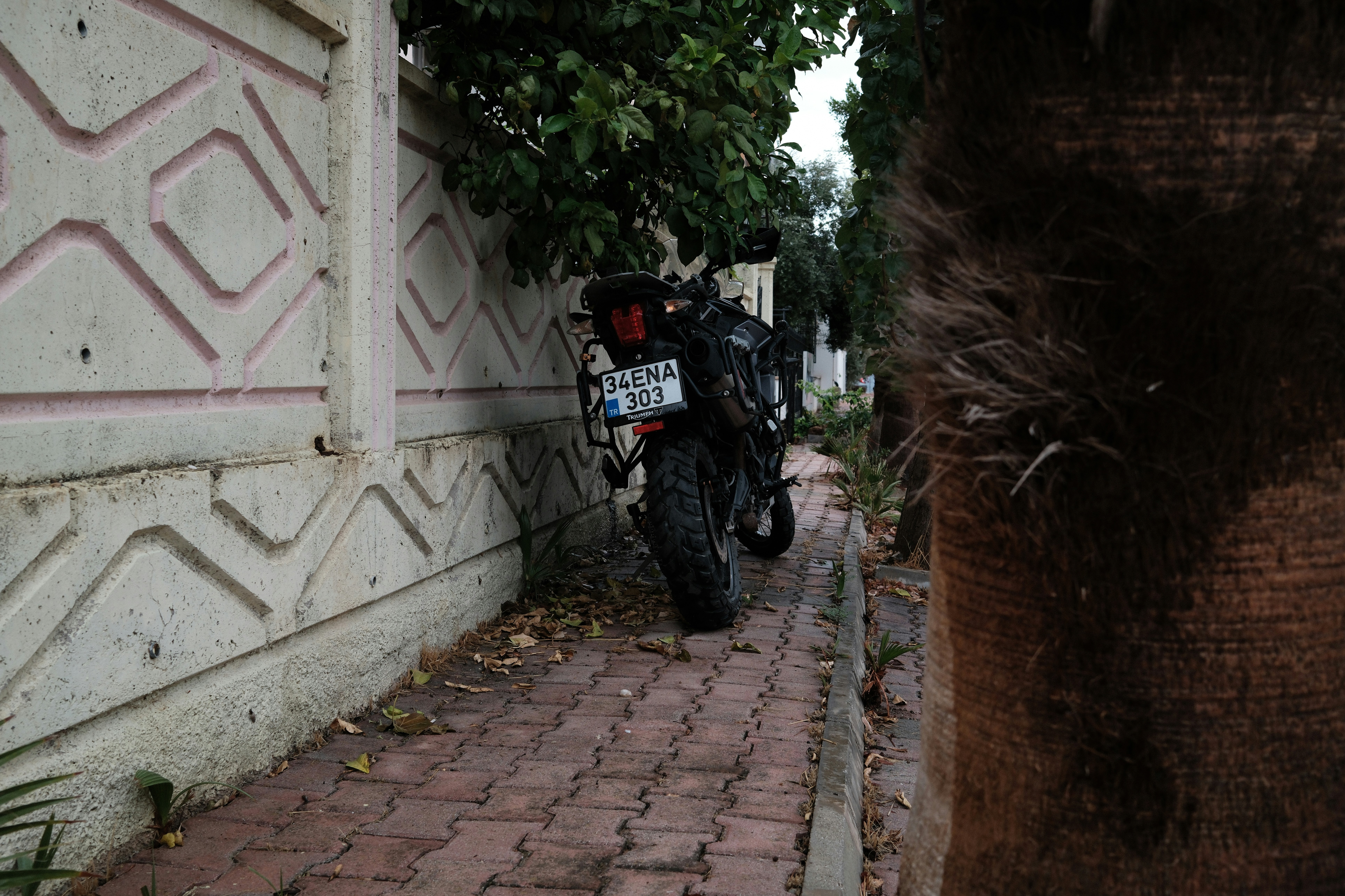 Sebuah sepeda motor hitam terparkir di trotoar beraspal di samping dinding beton bermotif
