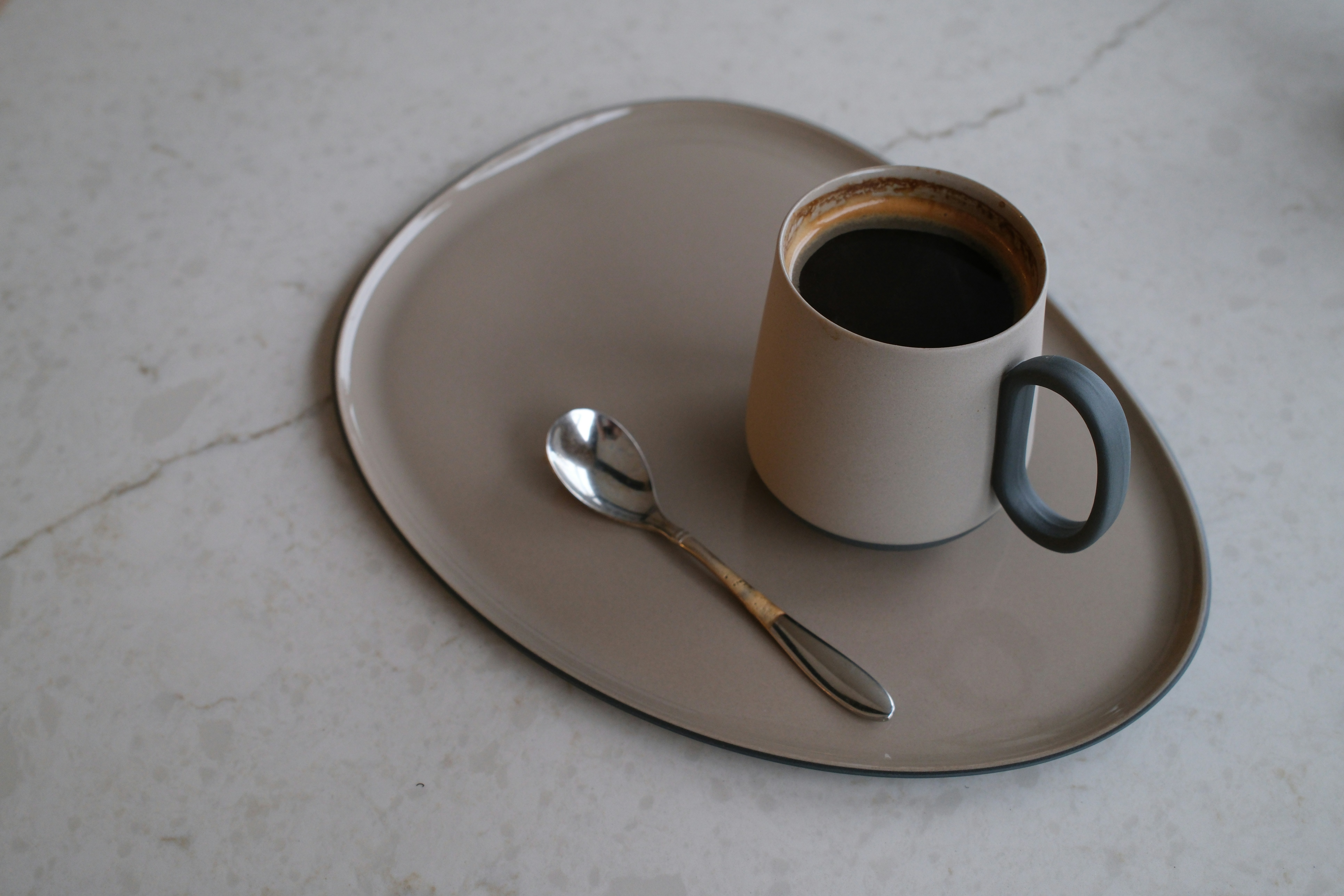 Secangkir kopi hitam dan sendok kecil di atas nampan oval krem