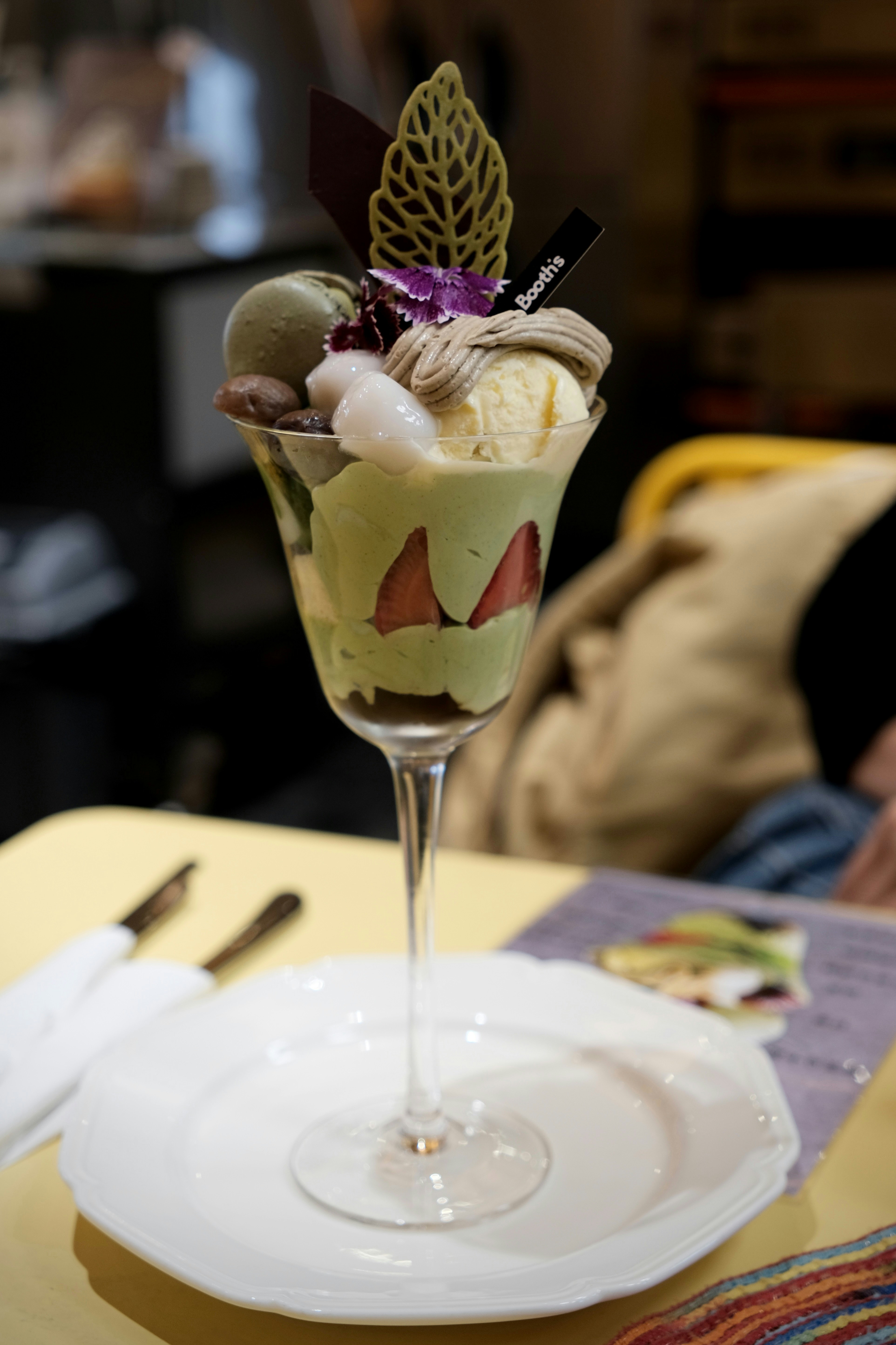 A matcha parfait with strawberries, mochi, and a macaron in a tall glass on a plate