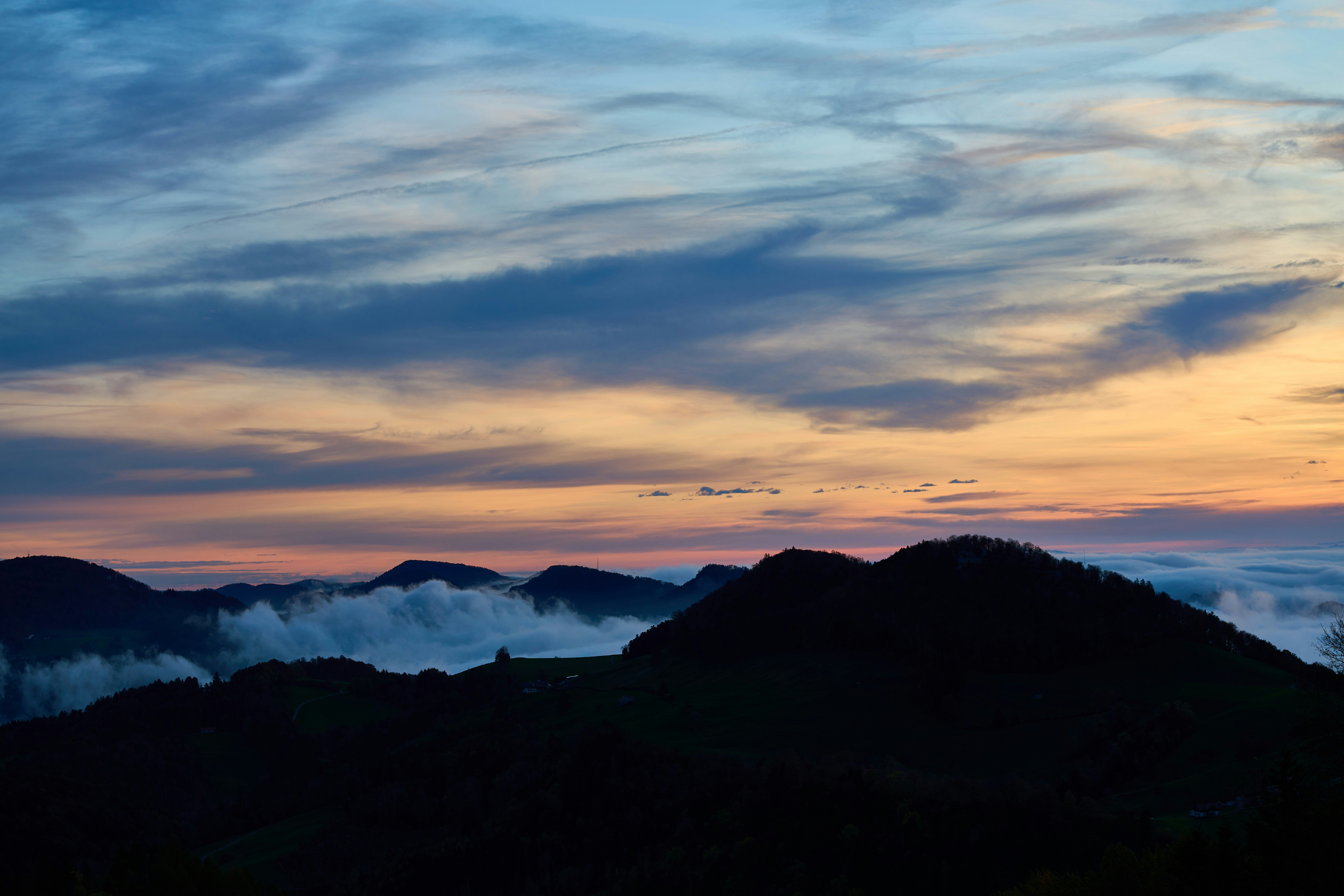 Silhouetted mountain ridges above a sea of clouds under a warm orange and blue sky