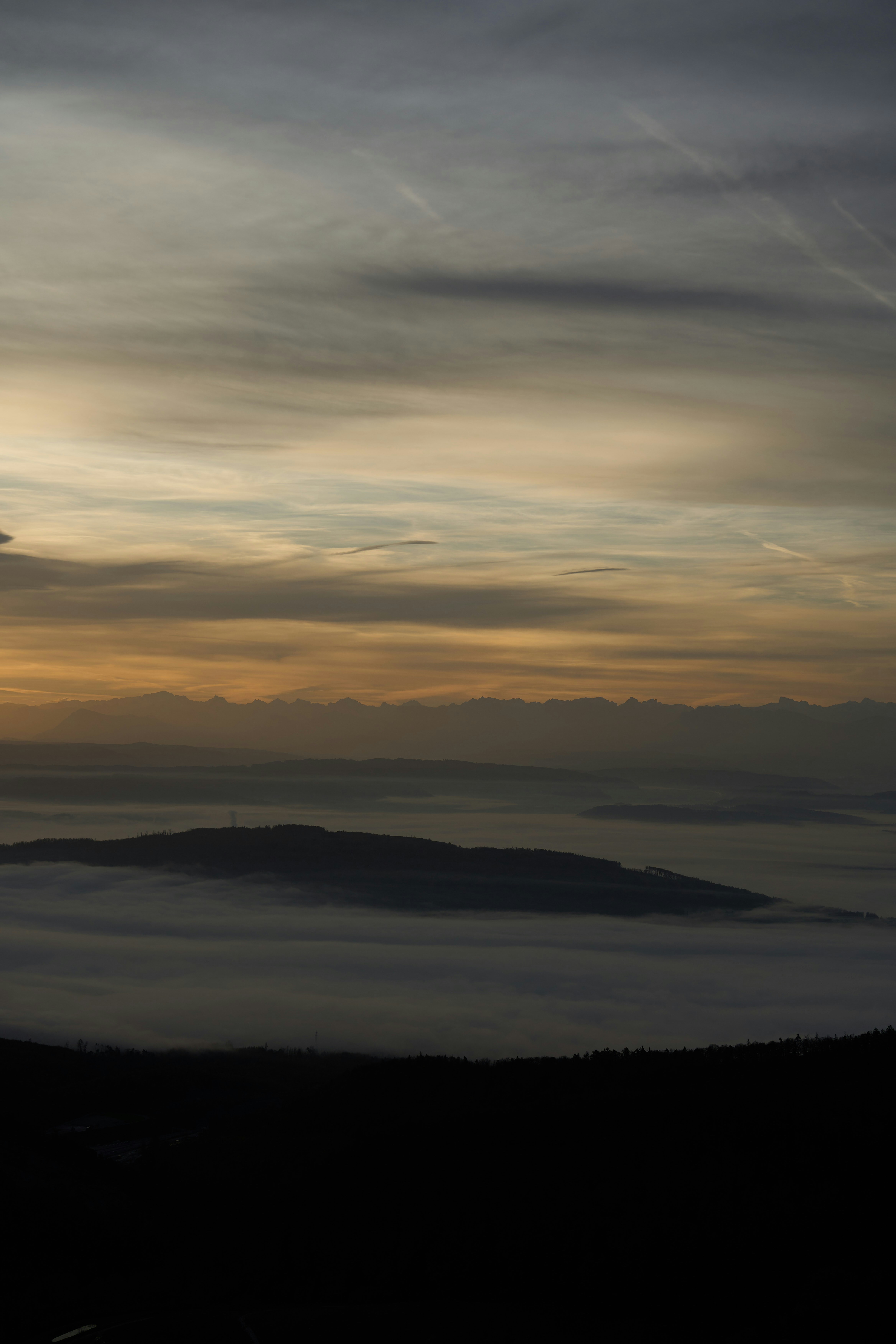 A distant mountain range silhouetted against a warm glowing sky above a thick layer of valley fog