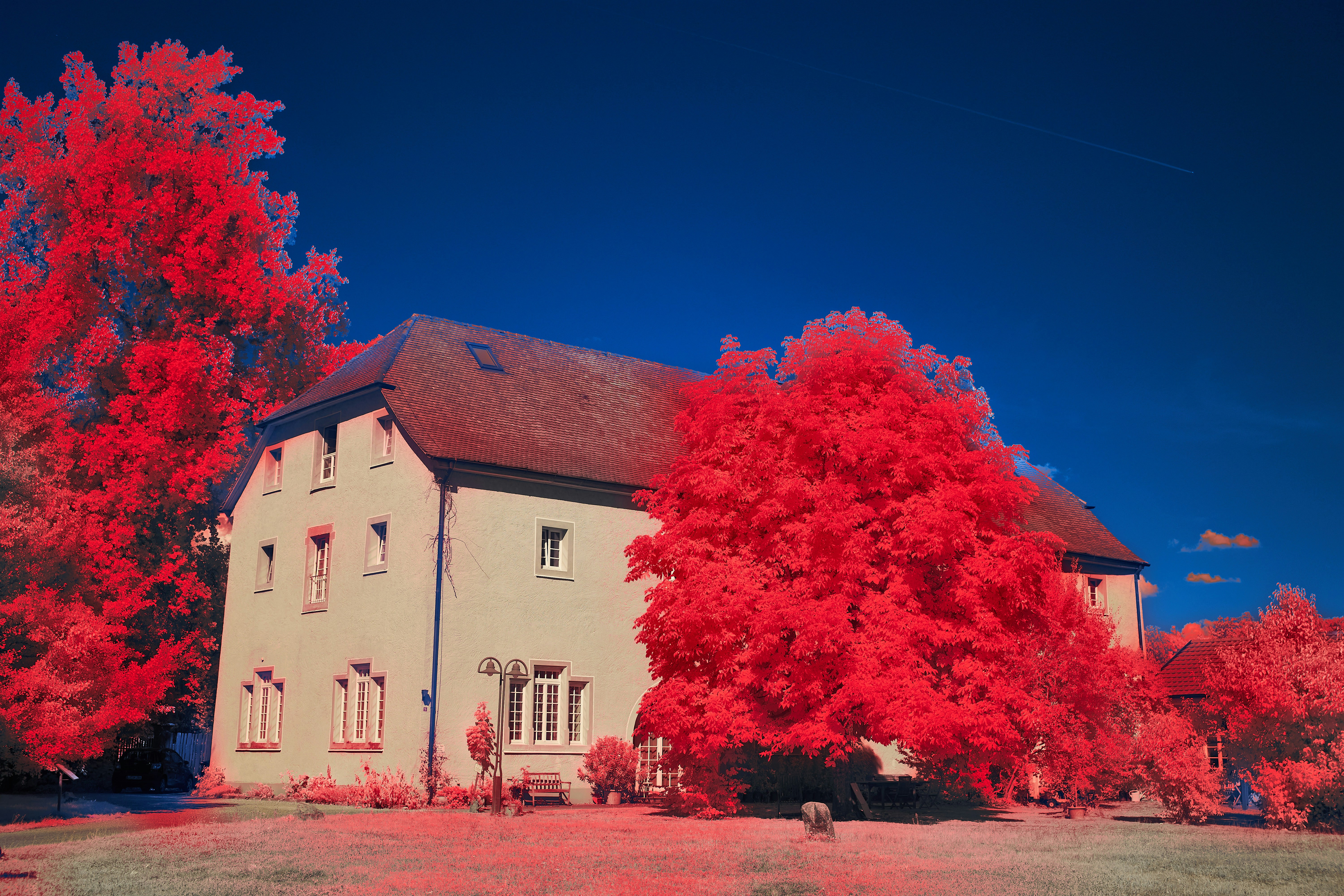 A large house with bright red foliage and a deep blue sky in an infrared photograph
