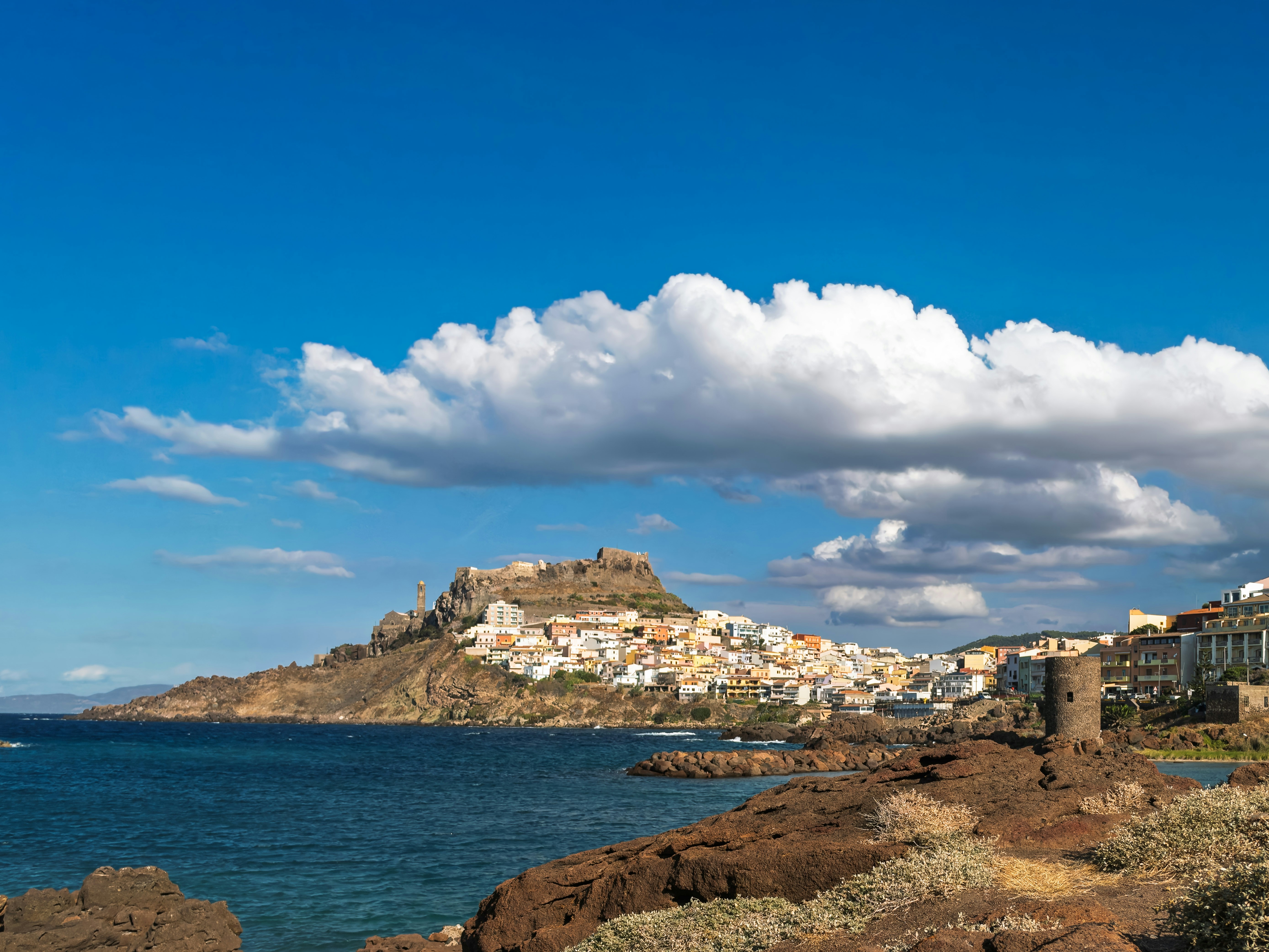 A coastal town with a hilltop castle overlooking the sea under a bright blue sky