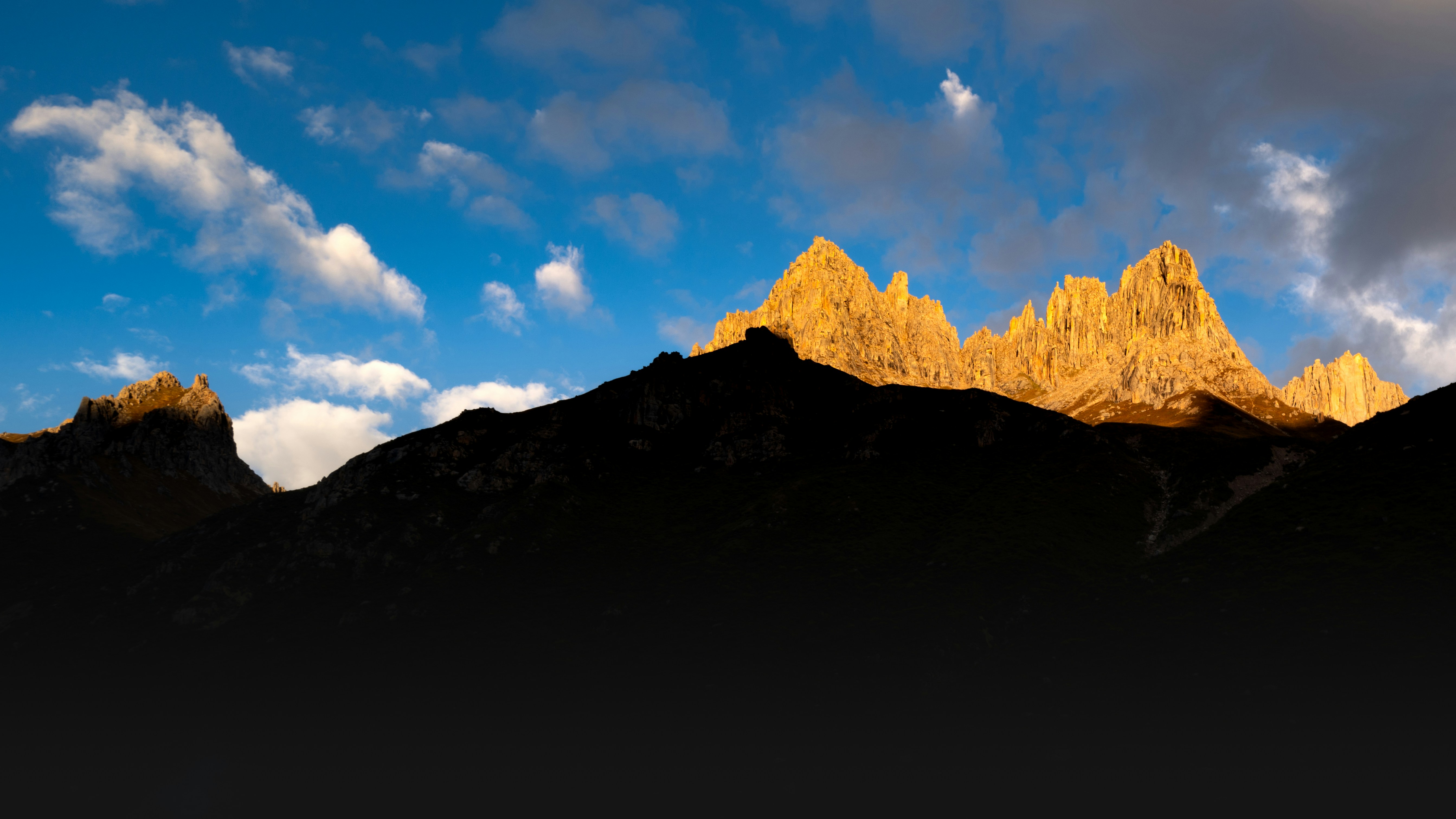 Jagged mountain peaks glowing in golden light above a dark silhouette against a blue sky