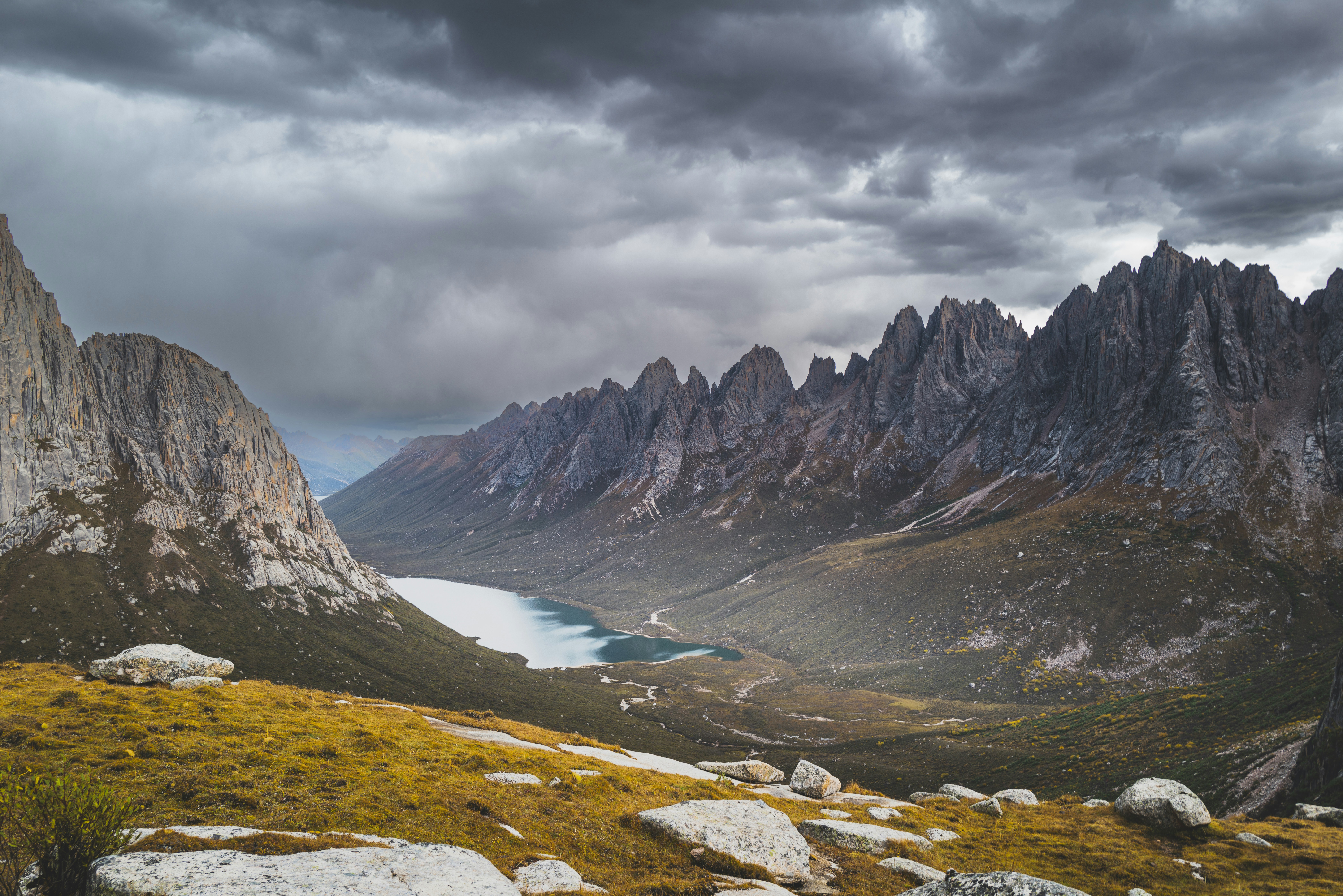 A glacial lake in a deep valley between jagged rocky mountain peaks under a cloudy sky