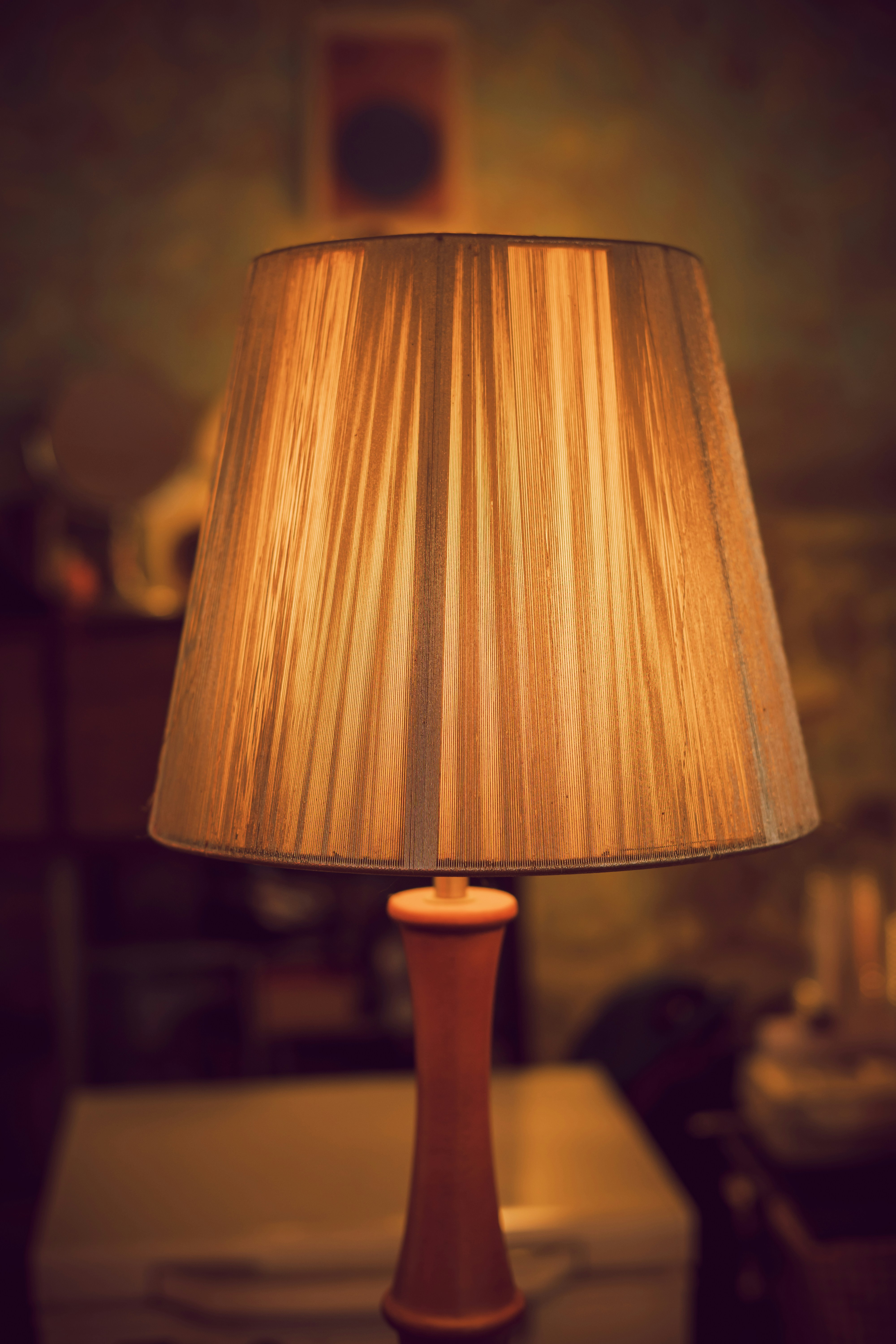 A lit table lamp with a pleated fabric shade in a dimly lit room