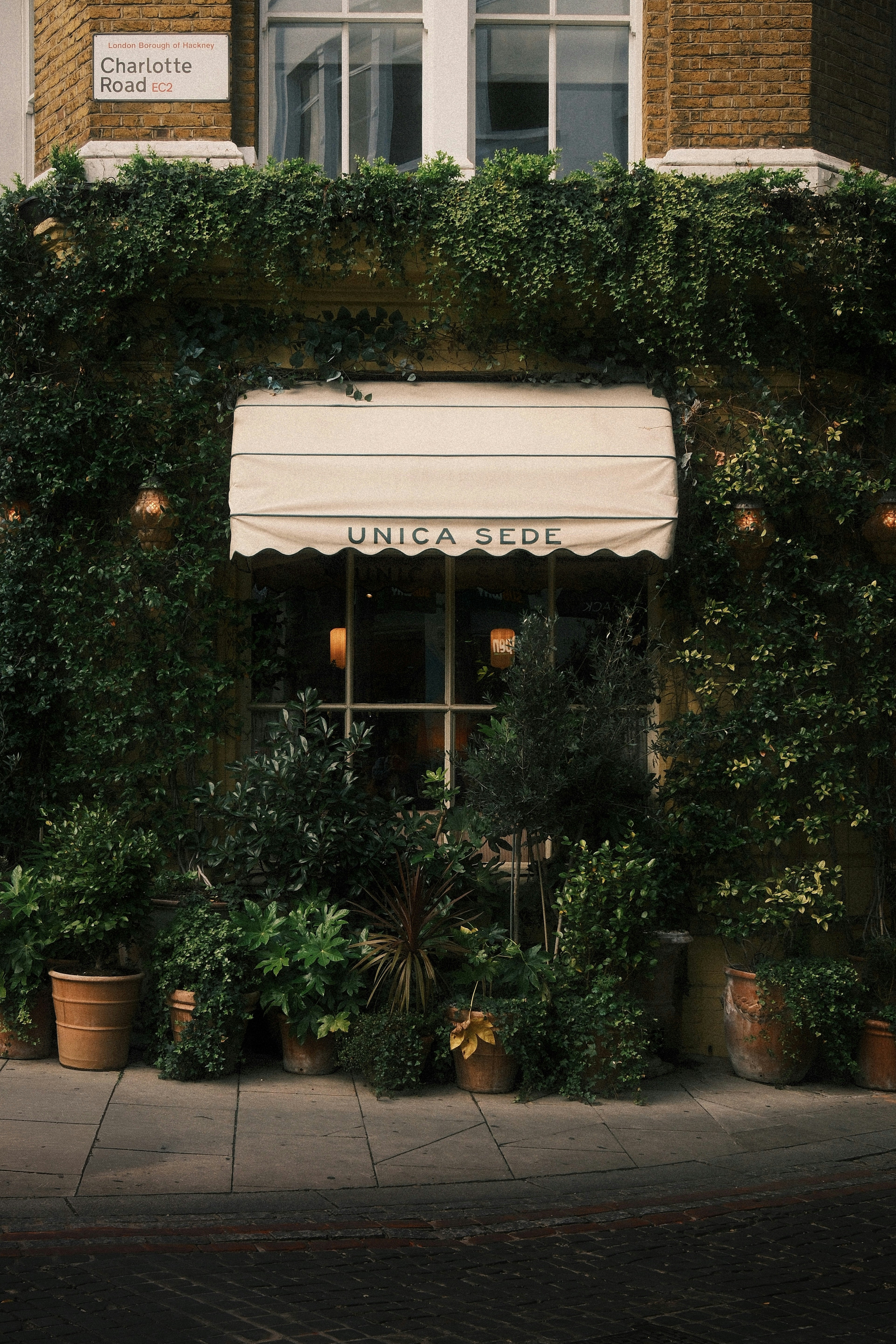 The ivy-covered facade of Unica Sede on Charlotte Road in London with potted plants