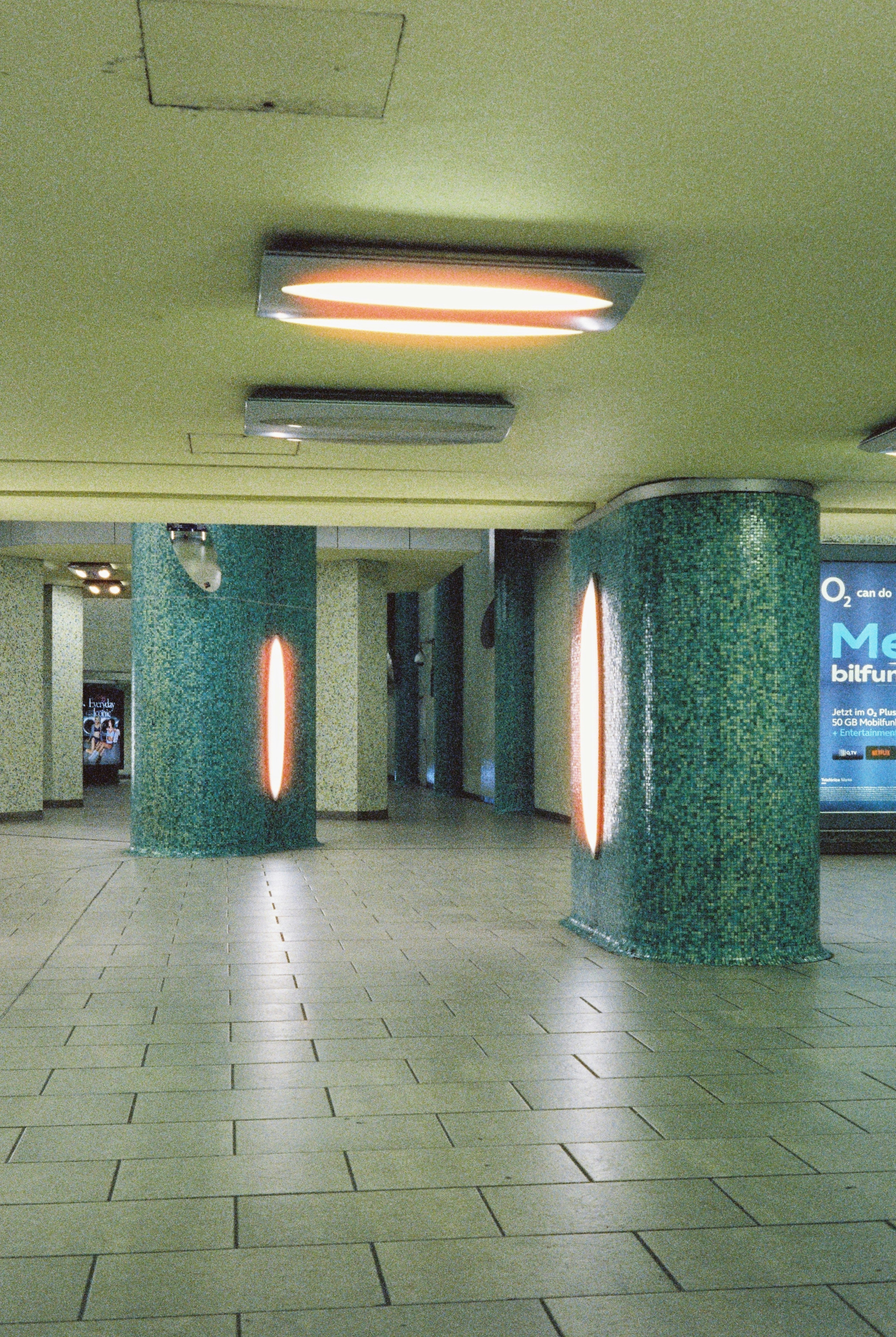 A subway station corridor with teal tiled pillars and warm glowing oval lights