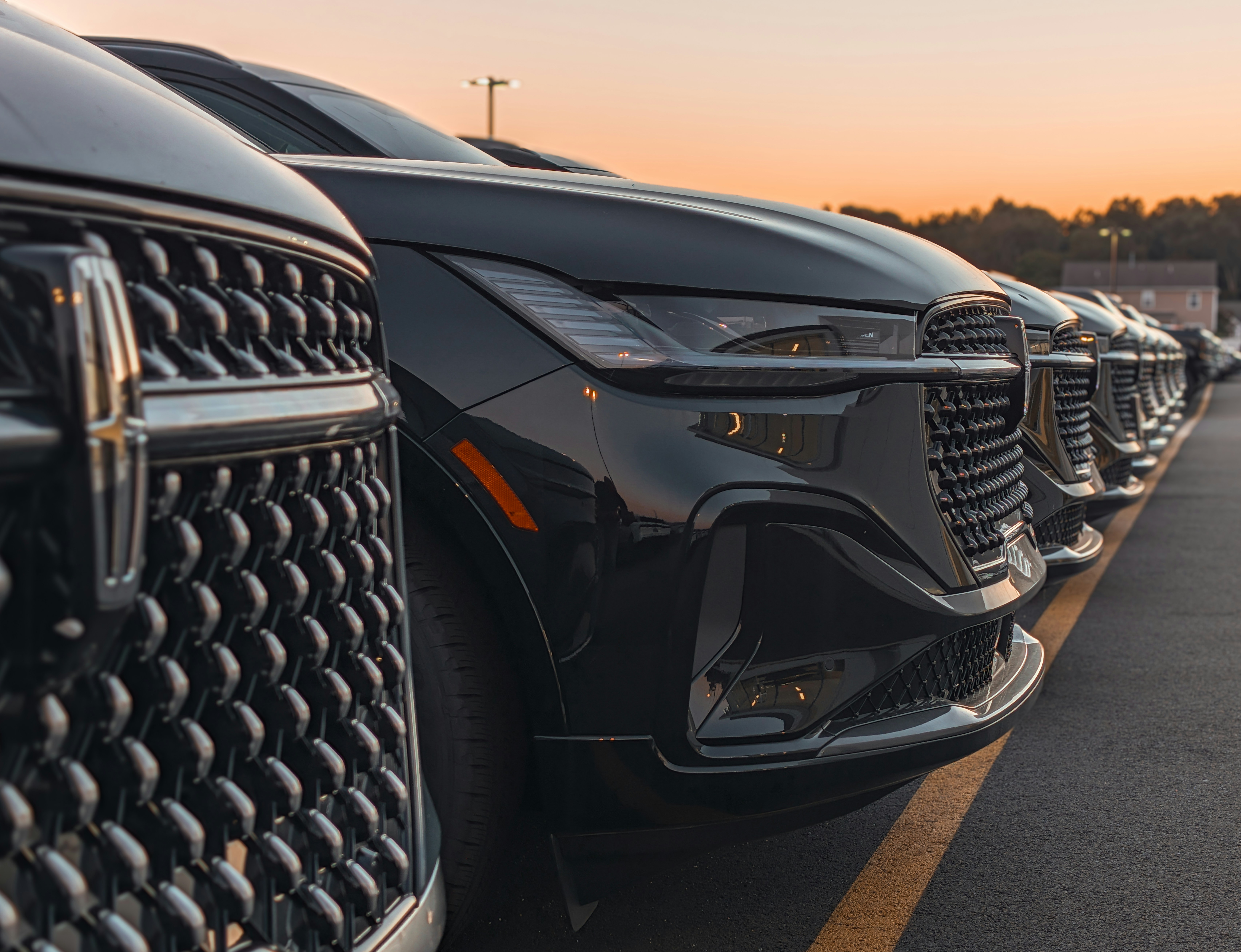 car dealership showroom - A row of black Lincoln SUVs parked on an asphalt lot during golden hour