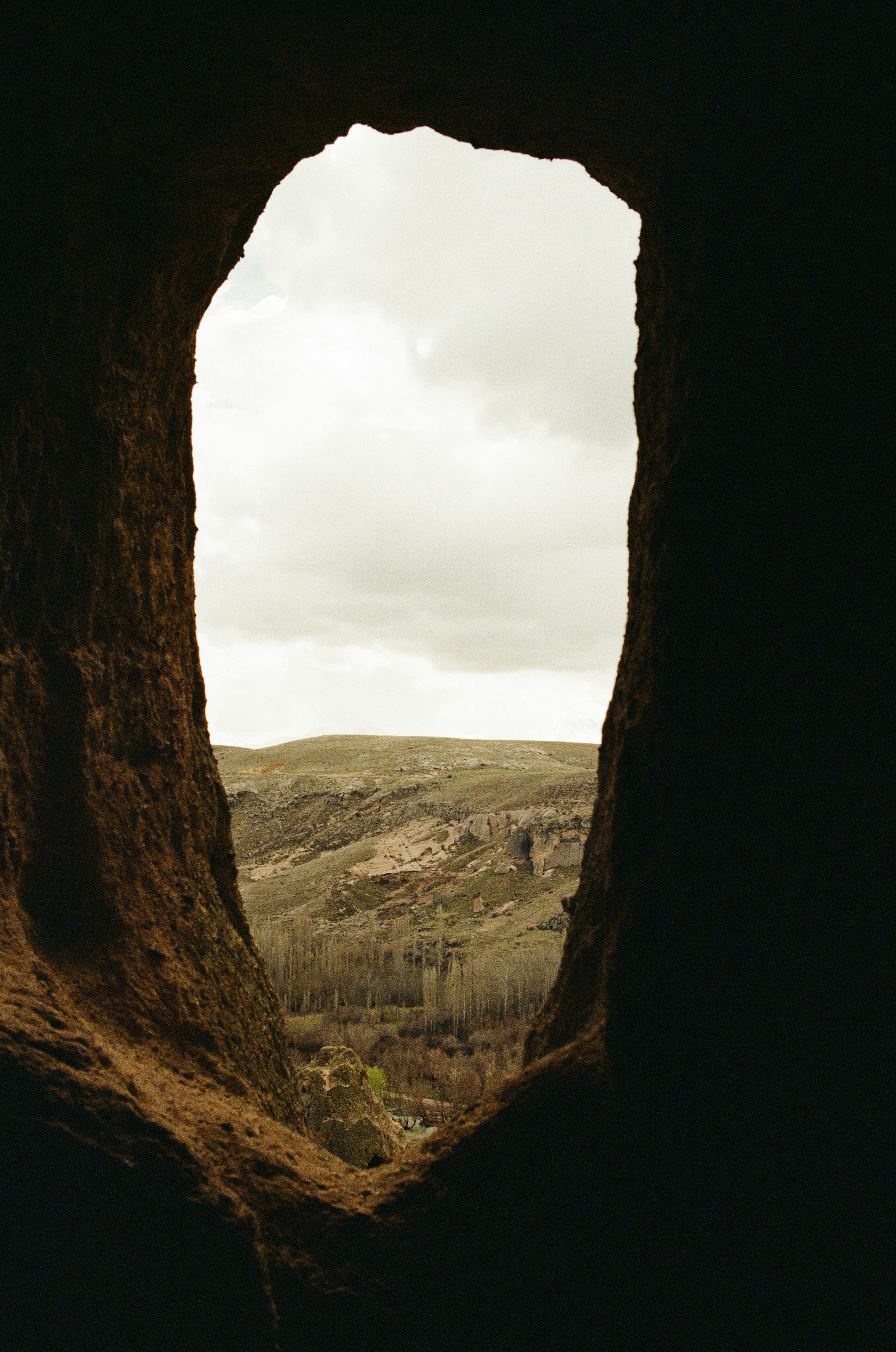 A view of a rocky valley and trees through a dark cave opening - 相关推荐