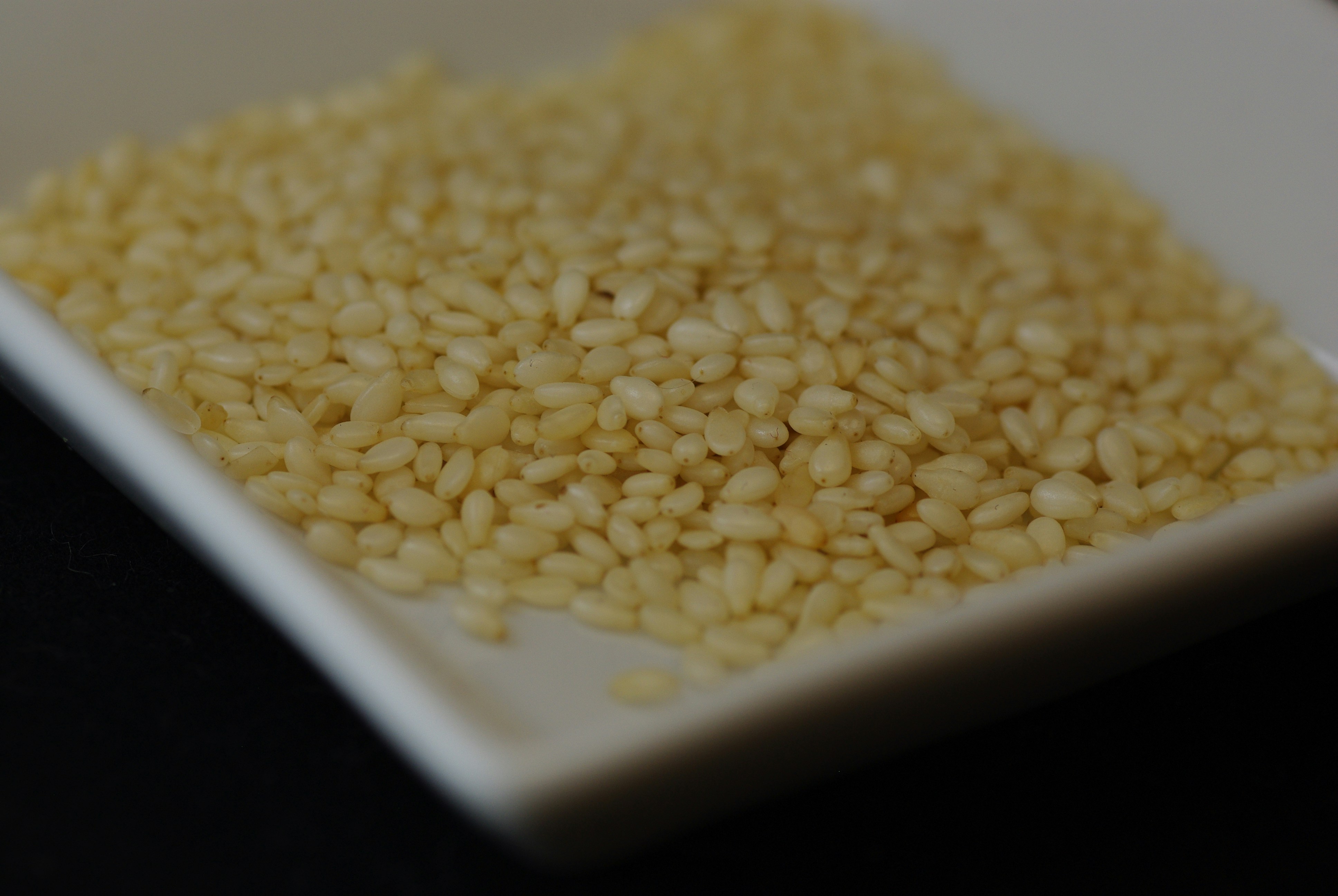 A pile of raw white sesame seeds in a small square white dish