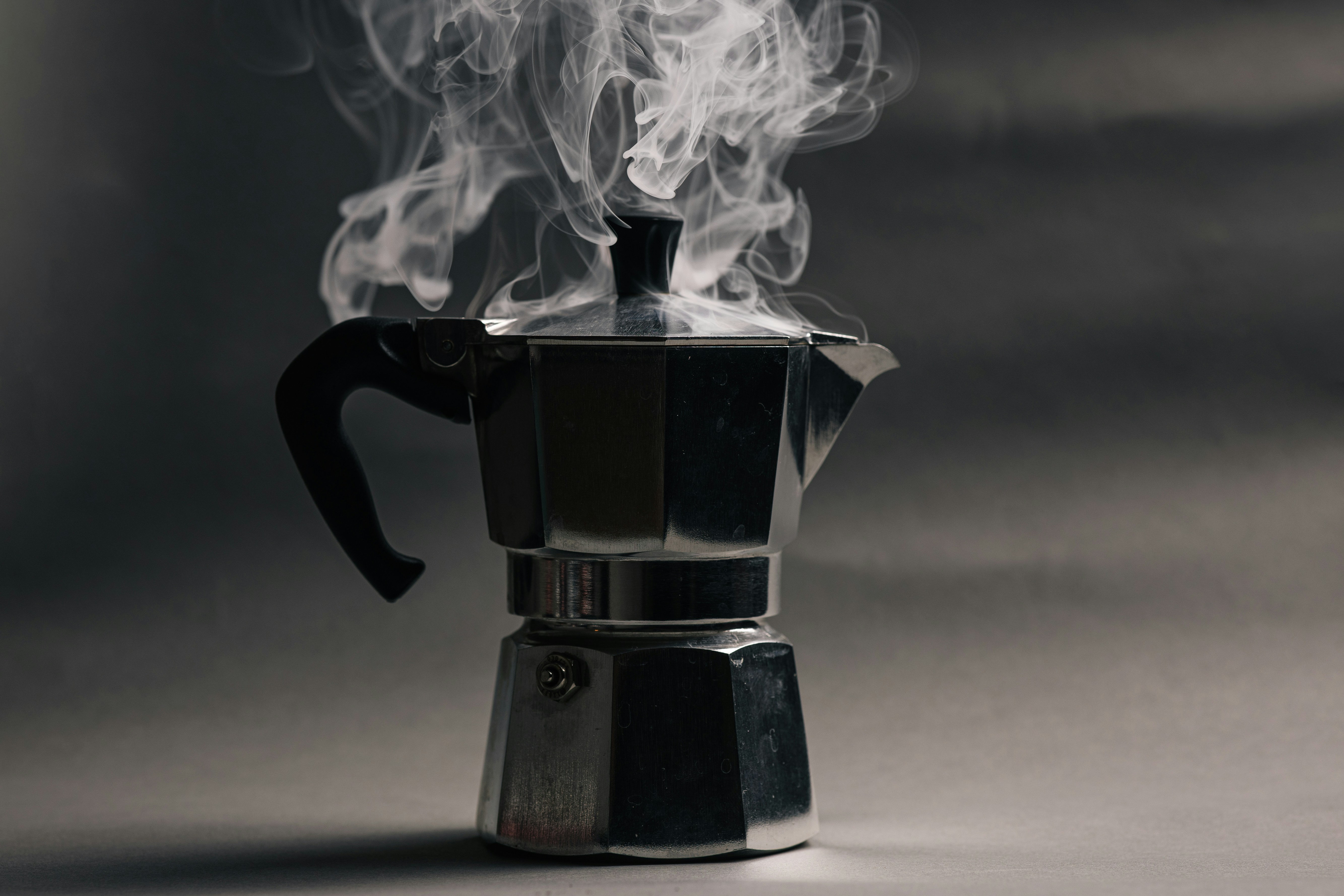 A steaming metal moka pot on a dark grey surface