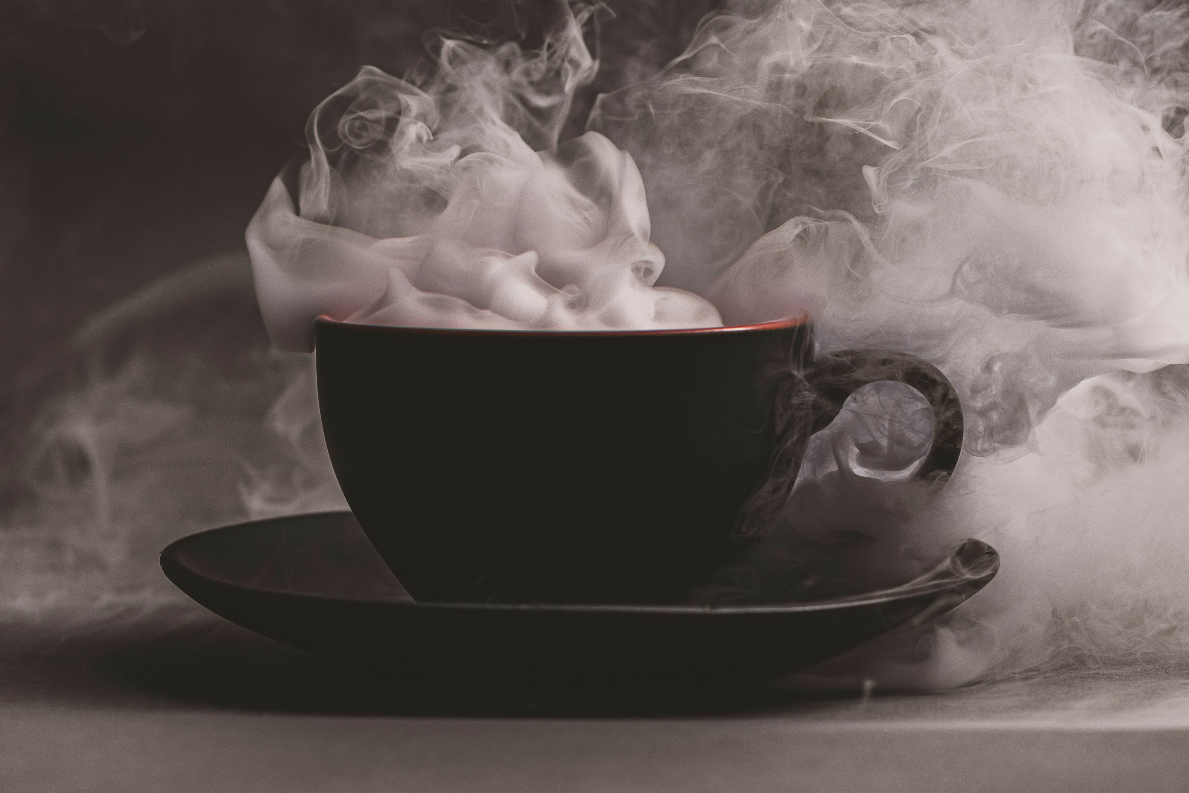A black coffee cup on a saucer surrounded by thick swirling white steam
