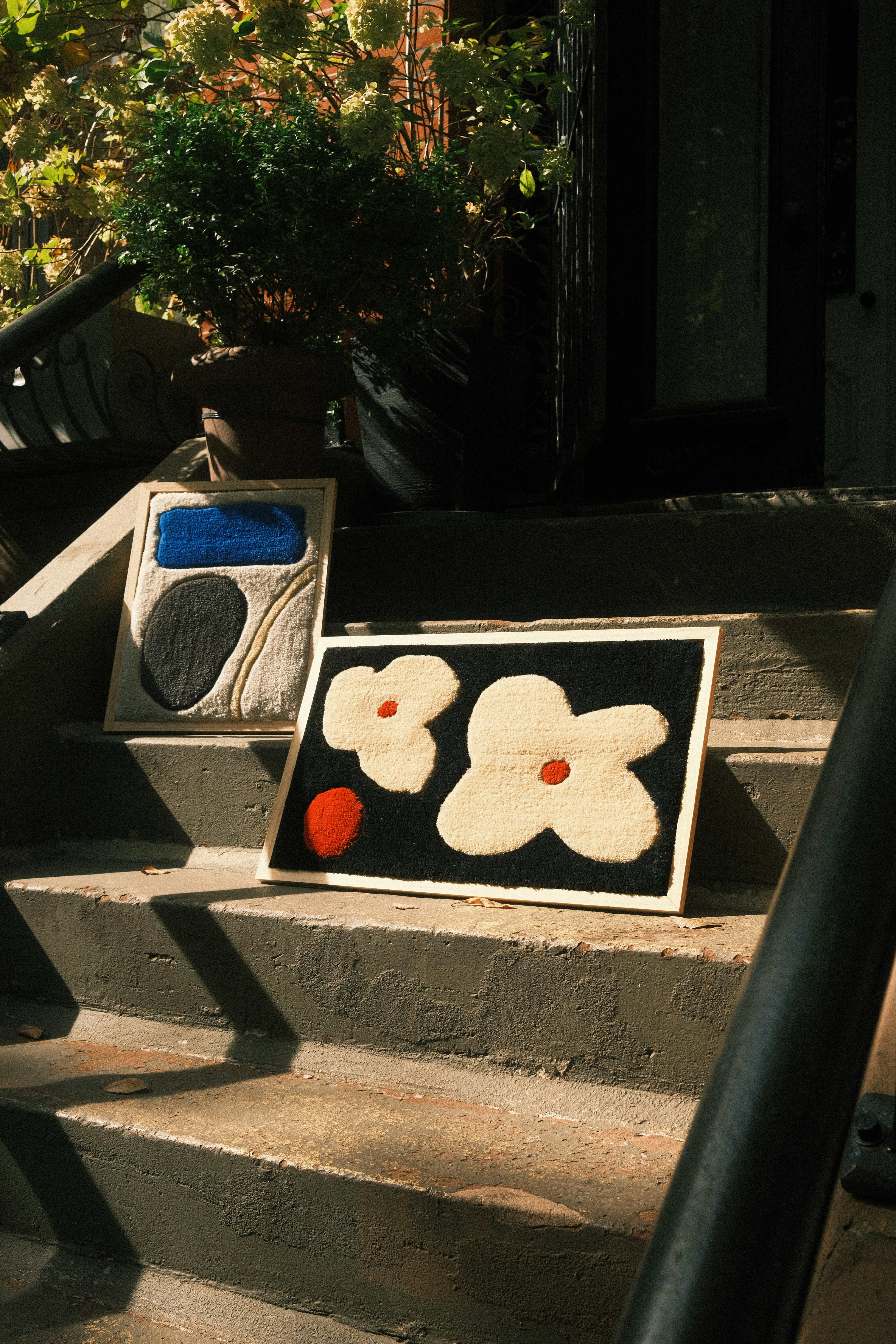 Two framed tufted textile art pieces with abstract floral and geometric shapes on concrete steps