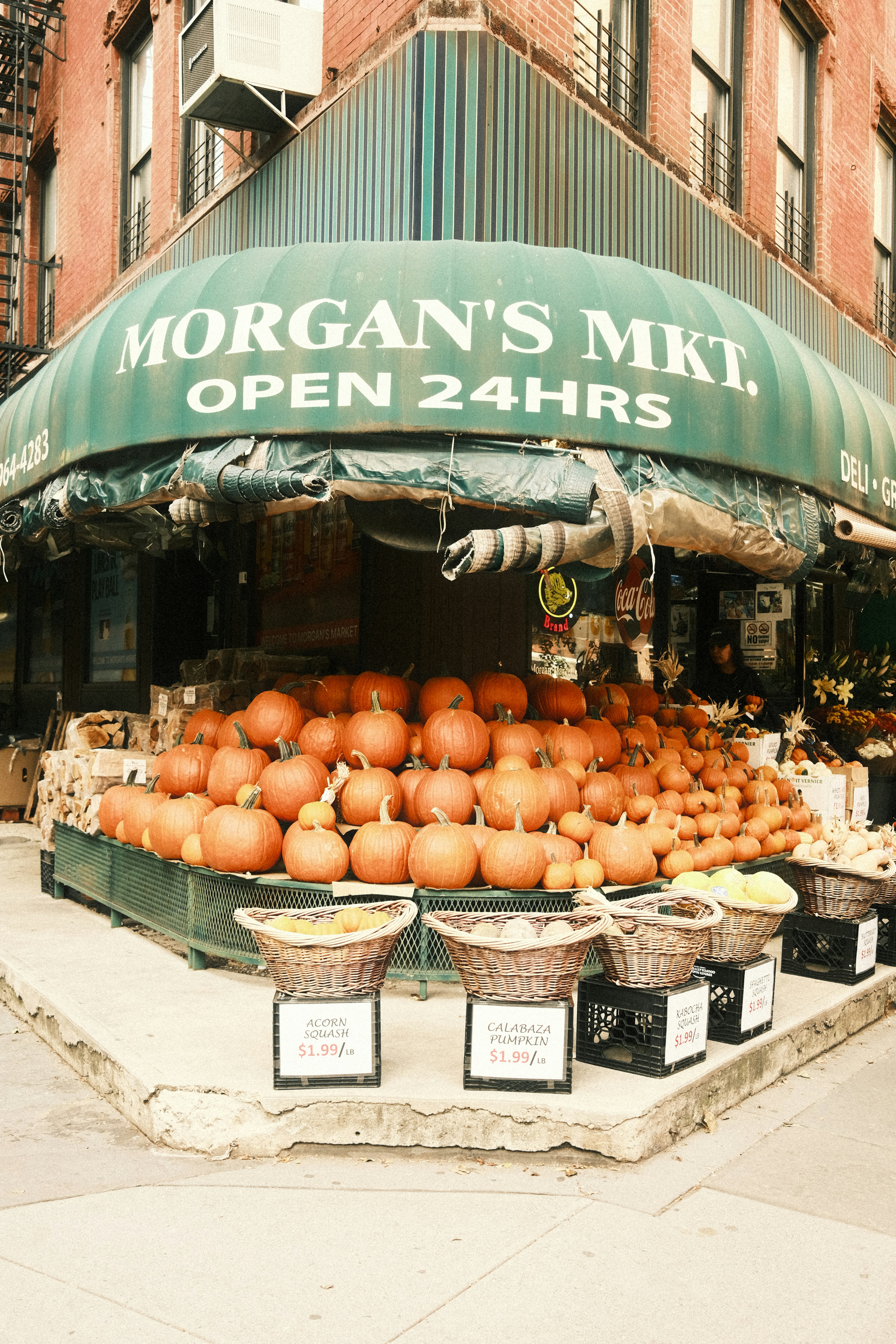 A large display of pumpkins and squash outside a corner market with a green awning