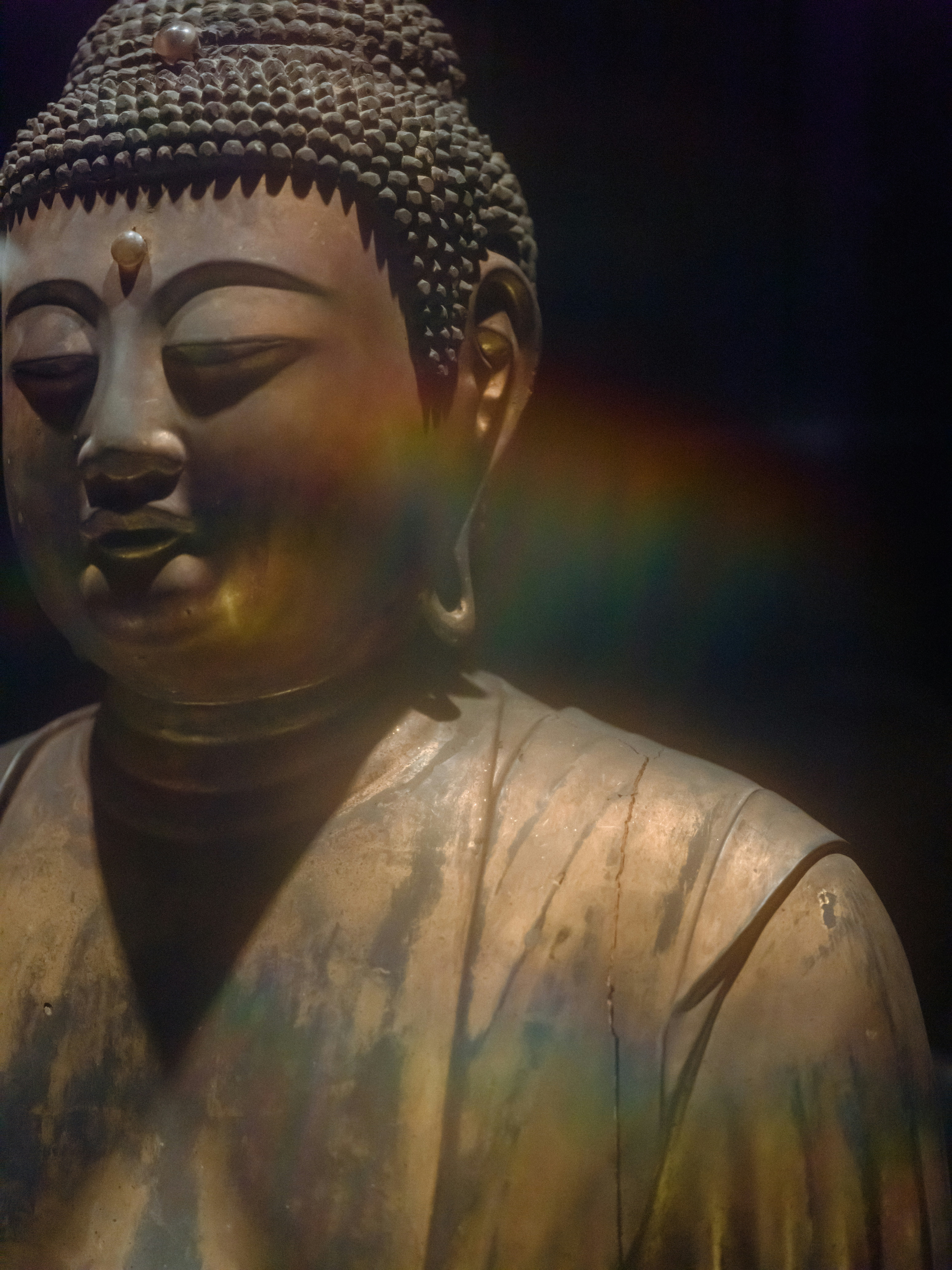 A bronze Buddha statue with a rainbow lens flare against a dark background