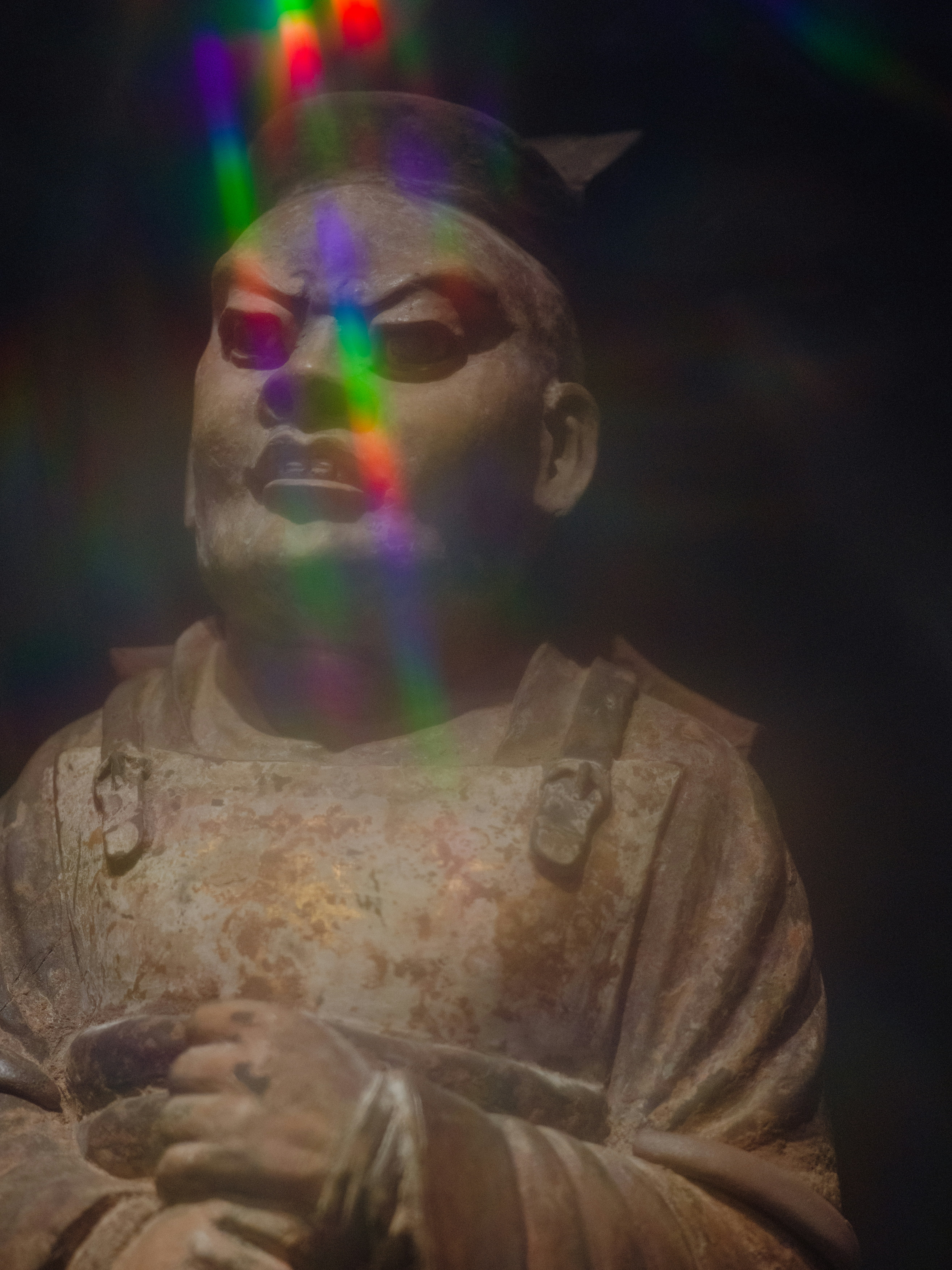 A weathered stone statue of a person in armor with a rainbow light flare