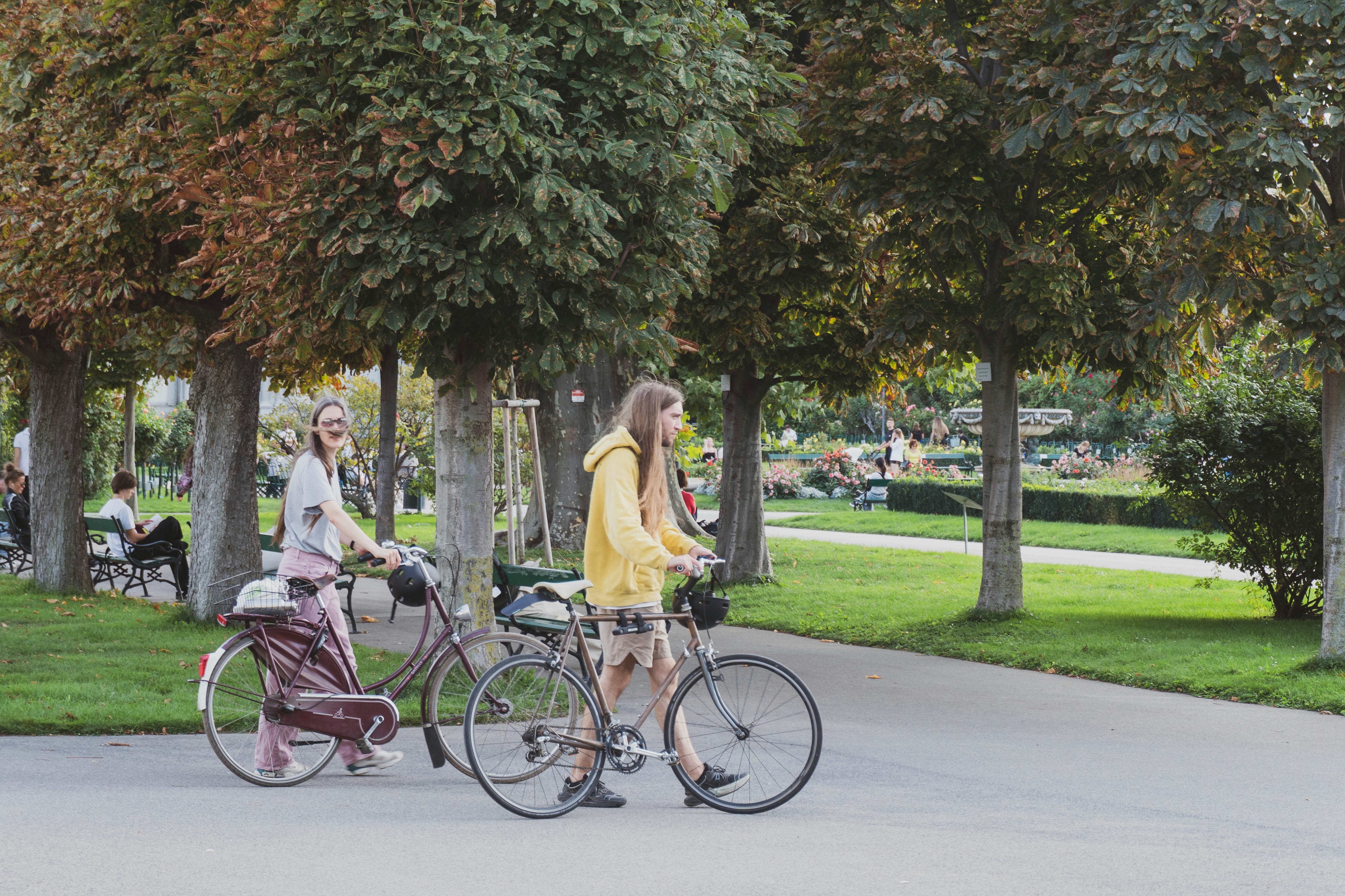 A woman and a man walking with bicycles through a tree-lined park in Paris