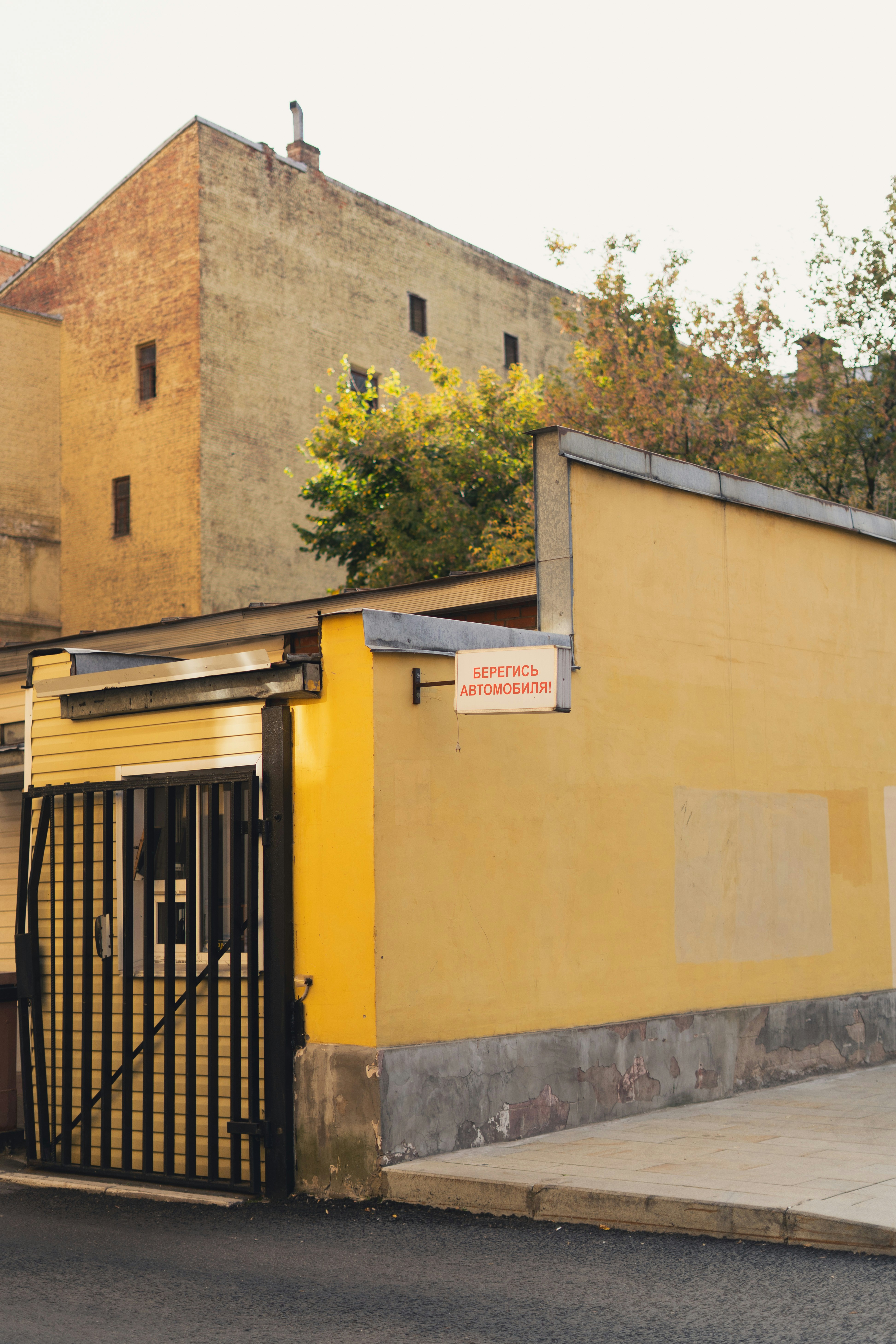 Un mur jaune avec un panneau indiquant « БЕРЕГИСЬ АВТОМОБИЛЯ ! » et une porte en métal noir