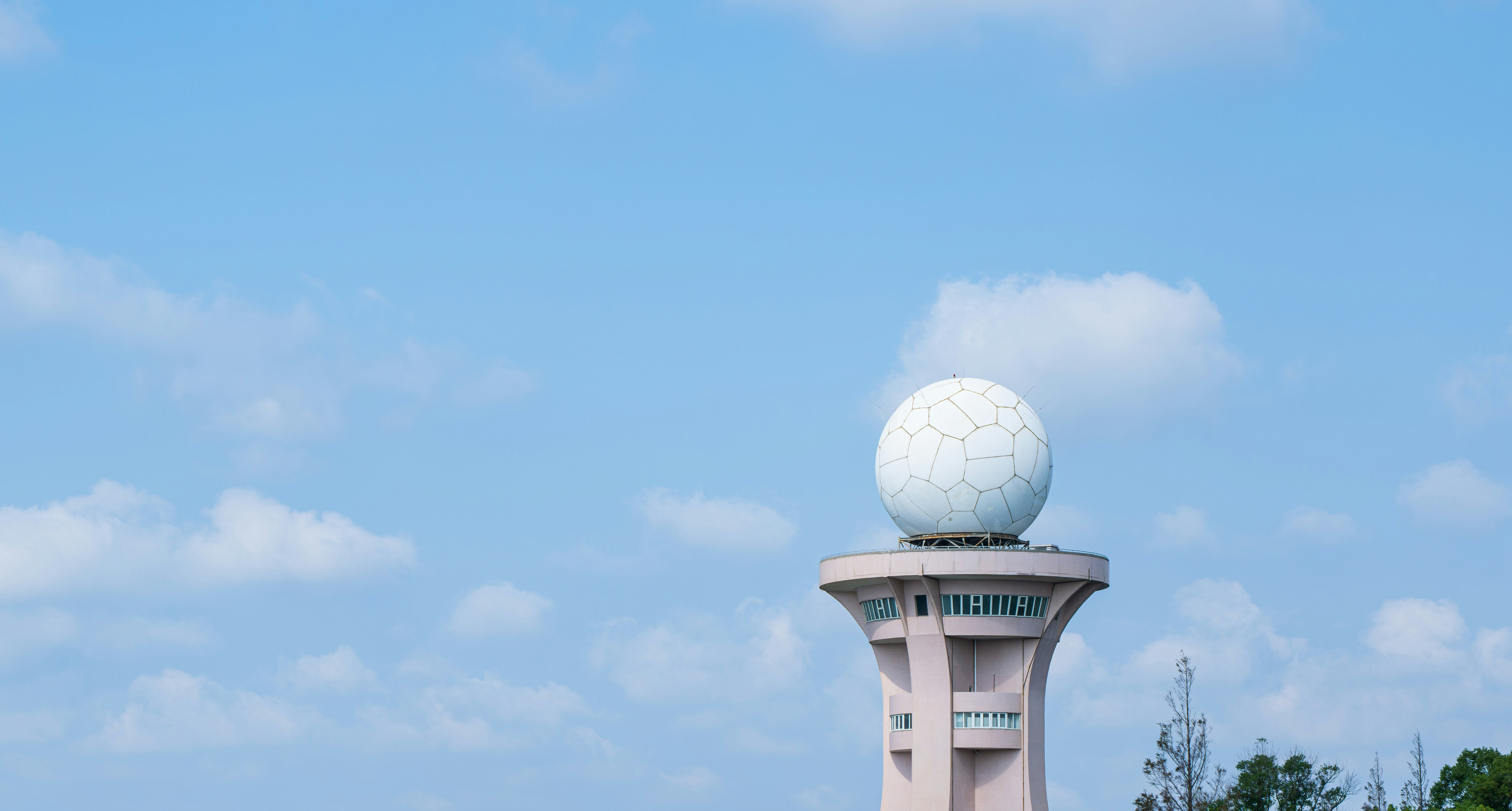 A white weather radar dome atop a tall pink concrete tower against a blue sky