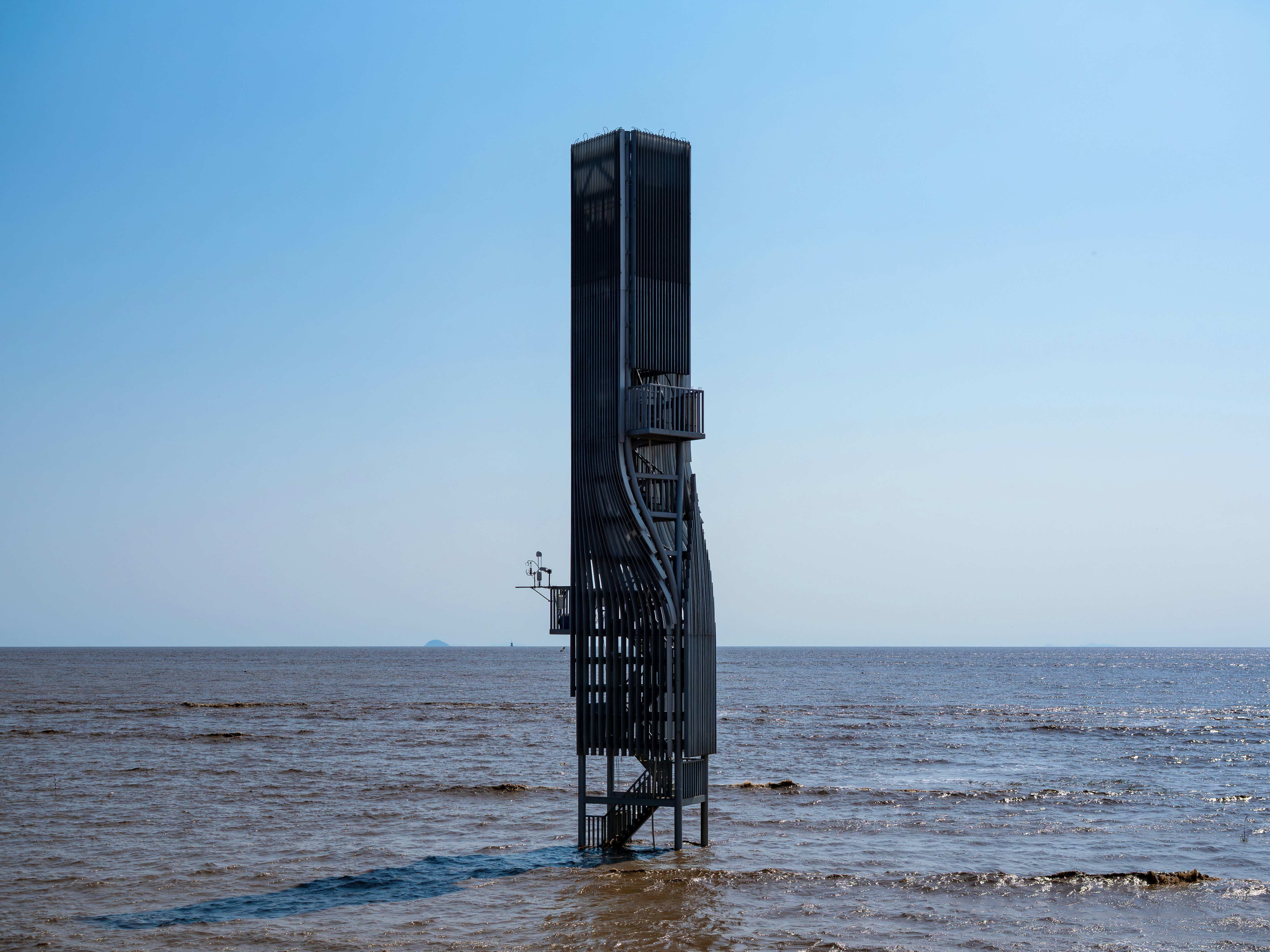 A tall metal observation tower standing in the middle of calm coastal water