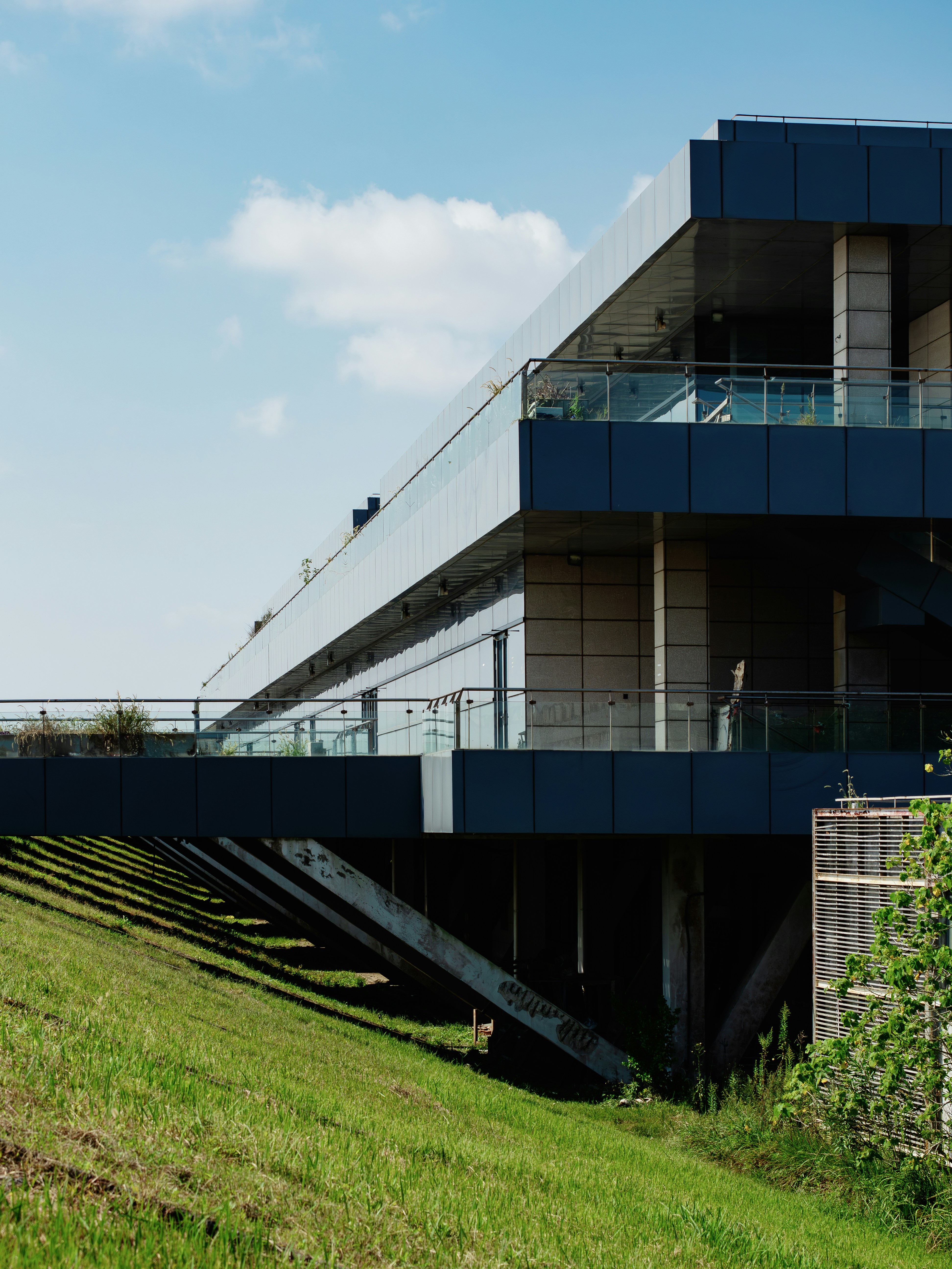 A modern building with dark blue panels and glass balconies cantilevered over a grassy slope