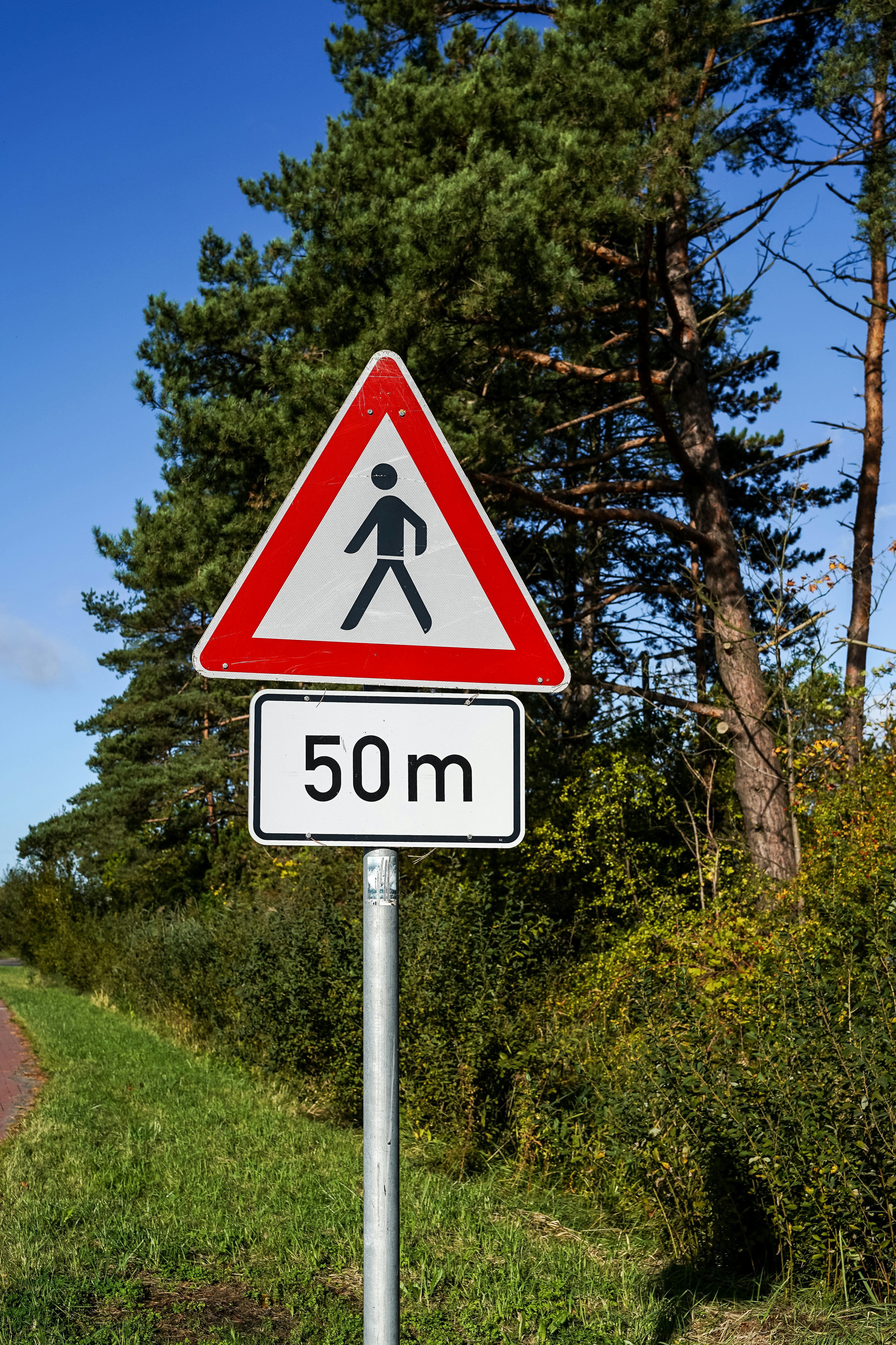 A triangular pedestrian crossing sign with a 50m distance plaque on a metal pole
