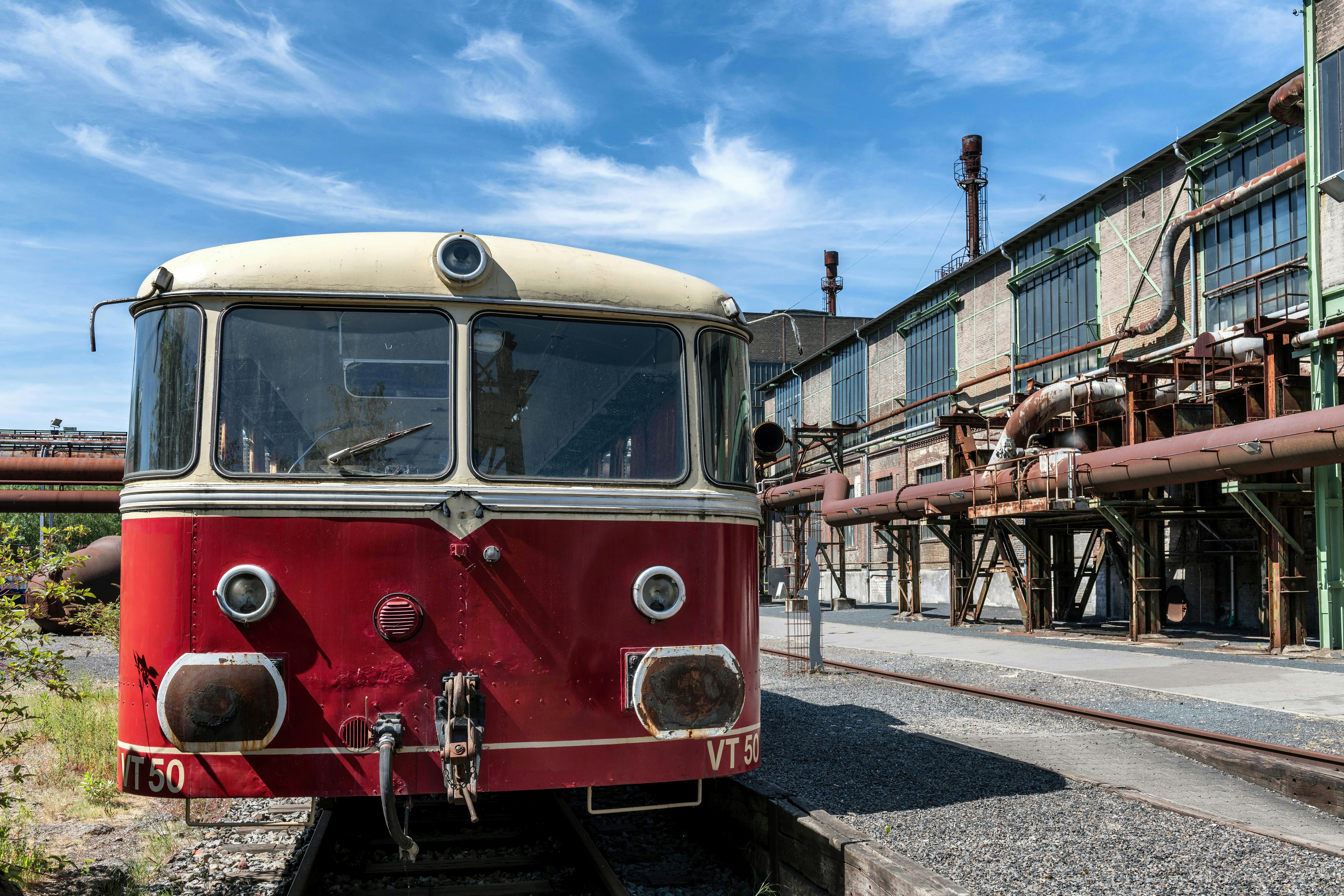 A vintage red and cream train carriage on tracks beside an industrial brick building