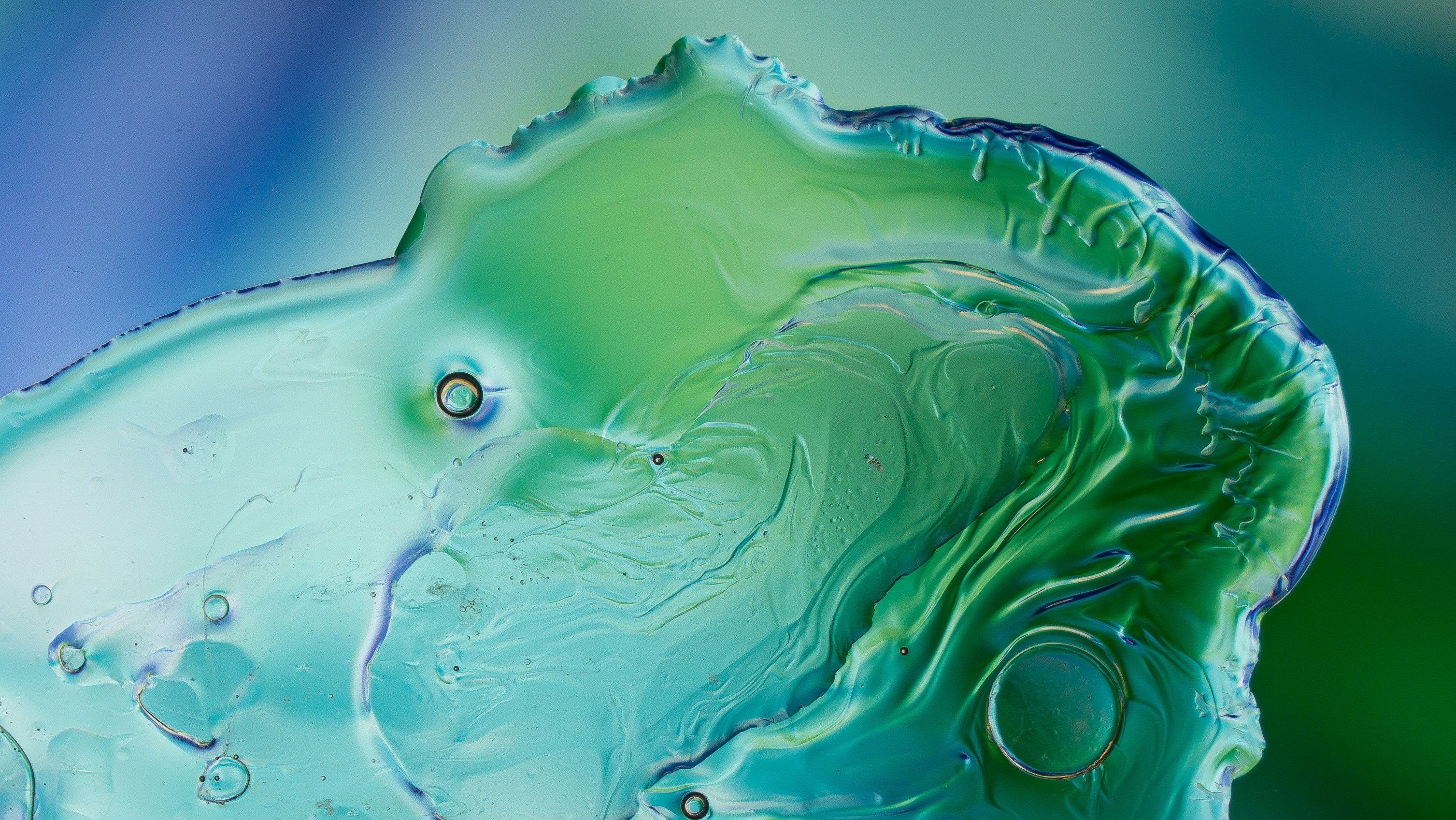 Macro view of swirling green and blue liquid with organic shapes and bubbles