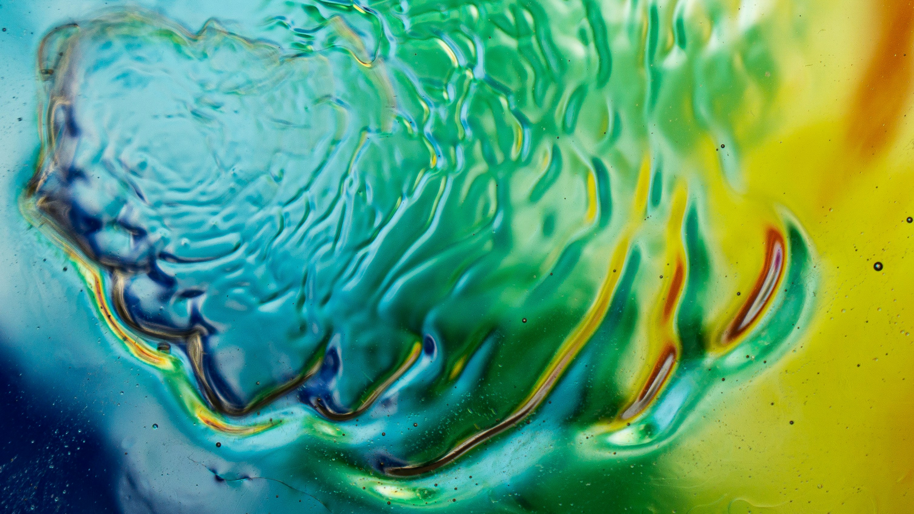 Abstract ripples of blue, green, and yellow liquid with light reflecting off the surface