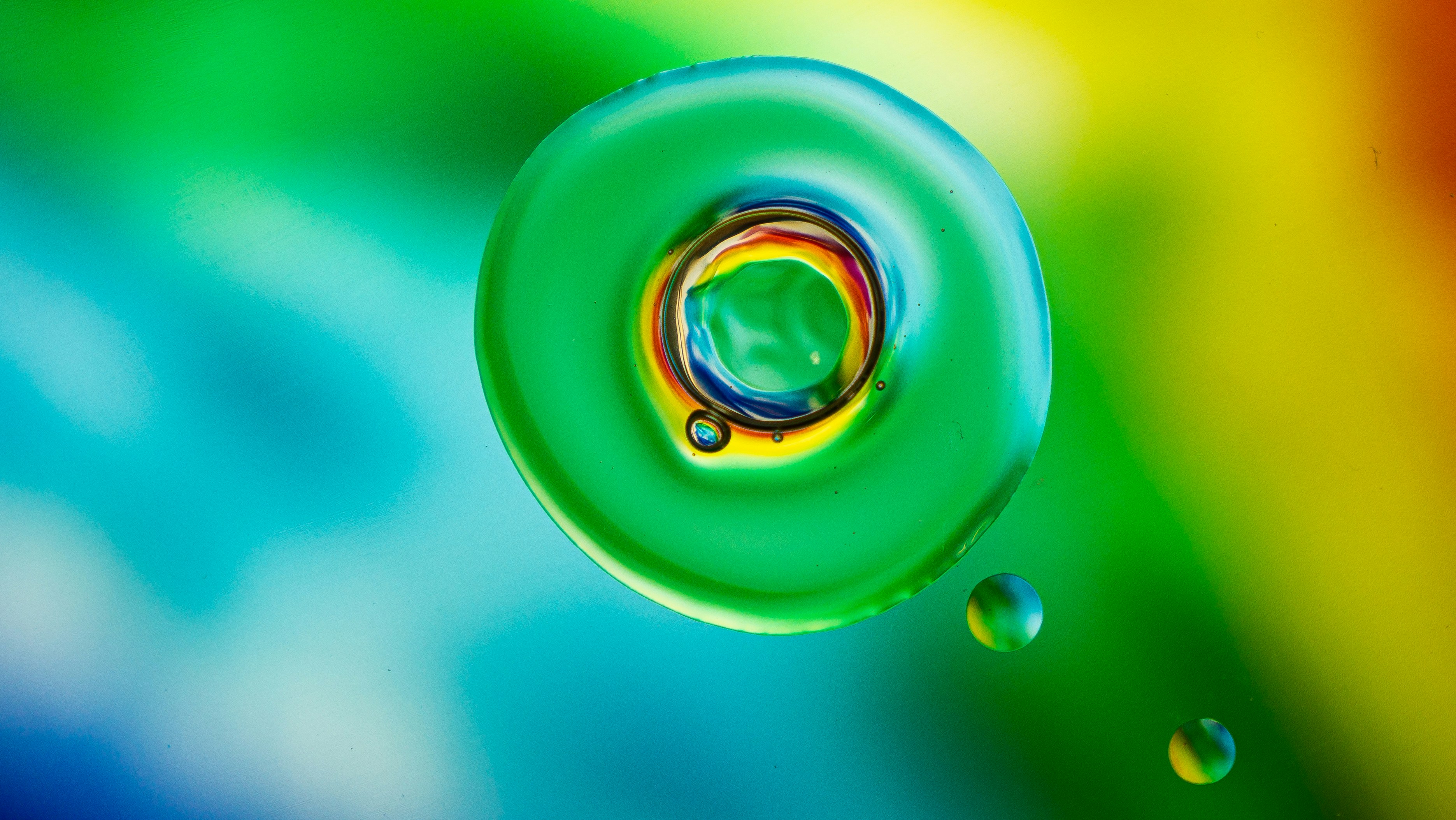 A macro view of a green oil droplet with rainbow light refraction on a colorful background