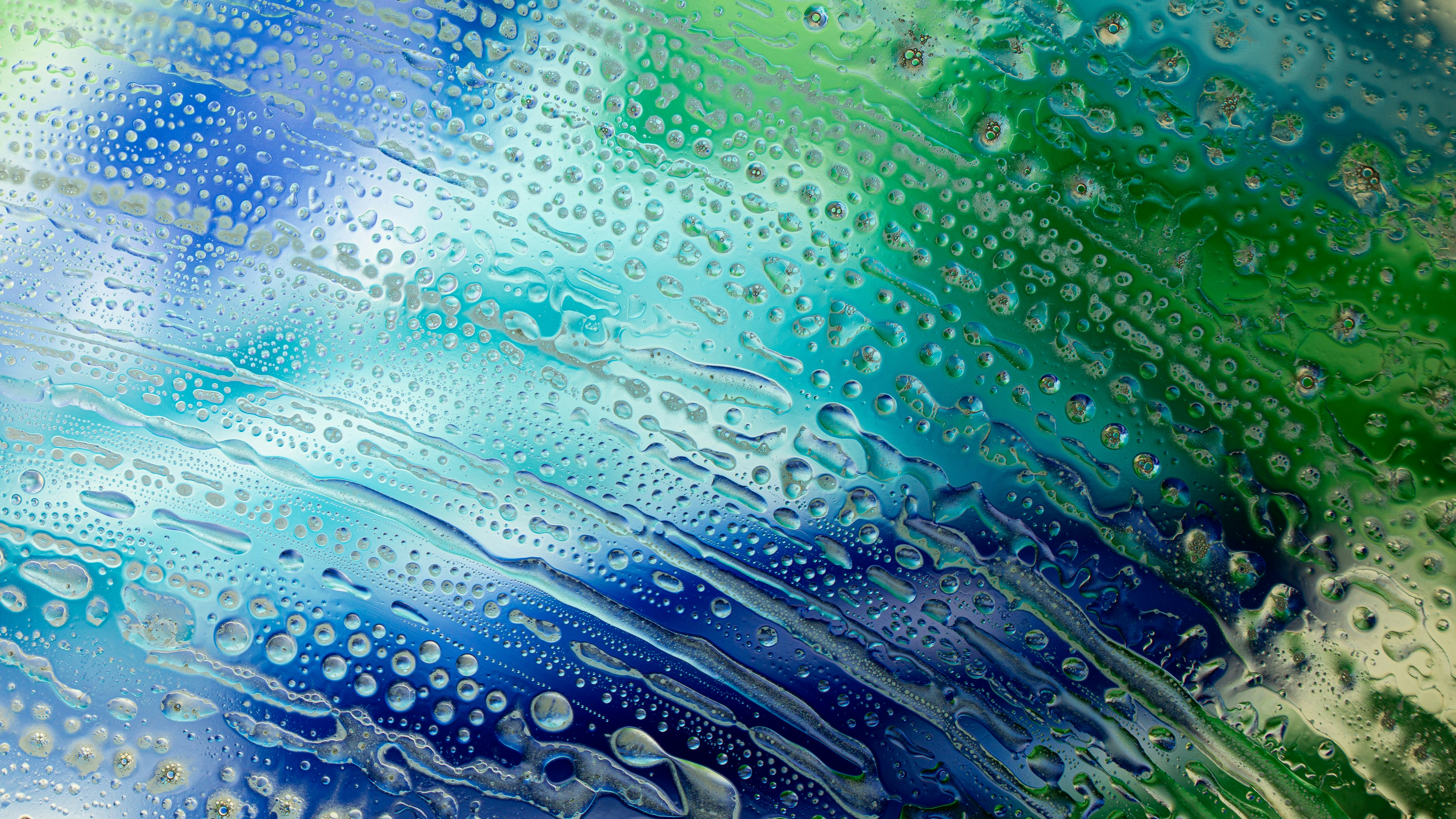 Water droplets and streaks on a glass surface with a blue and green gradient