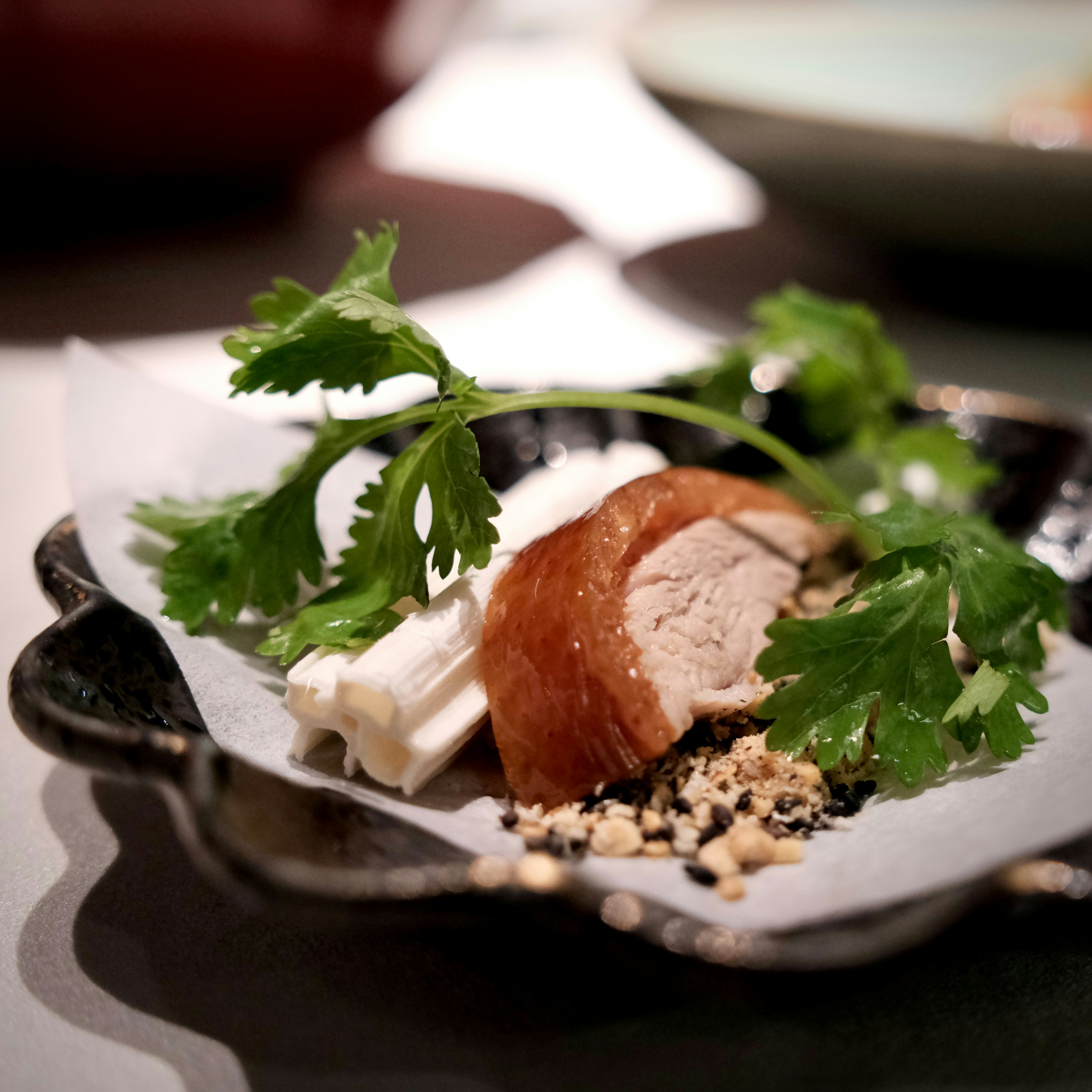 A slice of roasted duck with a white vegetable and cilantro on a small plate