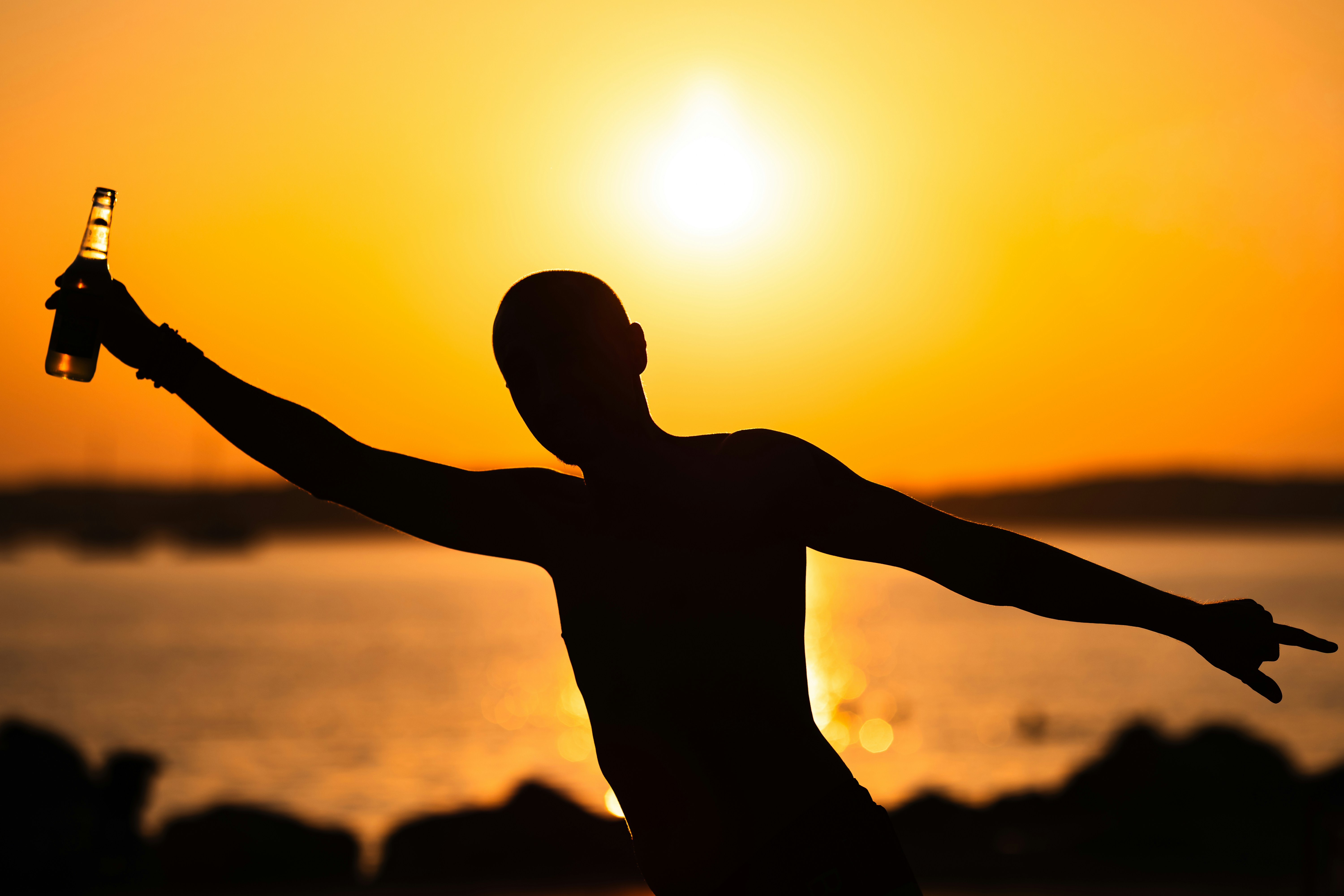 A person in silhouette holding a bottle against a bright golden hour sky