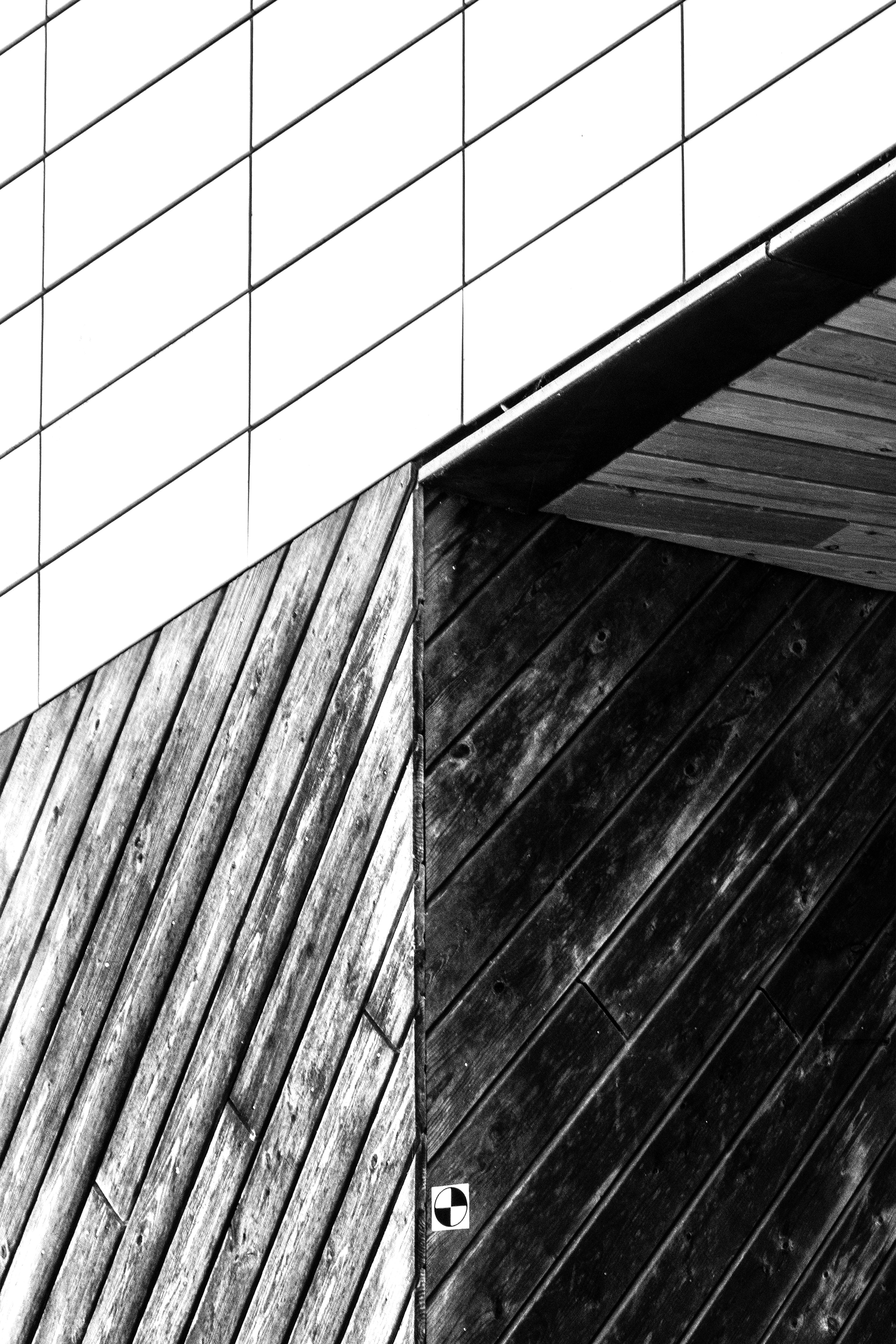 Detail arsitektur hitam putih dari papan kayu diagonal yang bertemu dengan dinding ubin