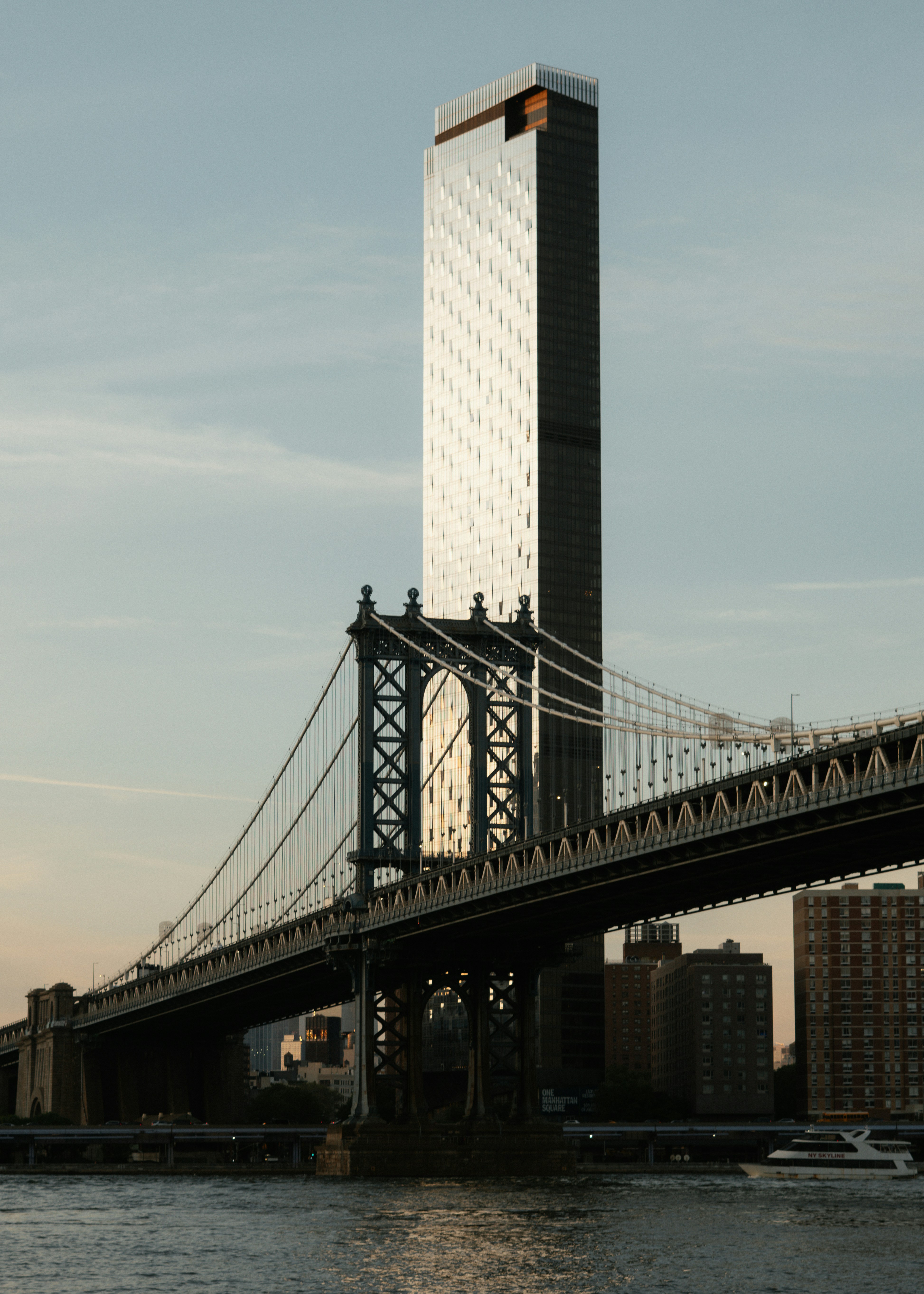 The Manhattan Bridge spanning the East River with a tall glass skyscraper in New York City