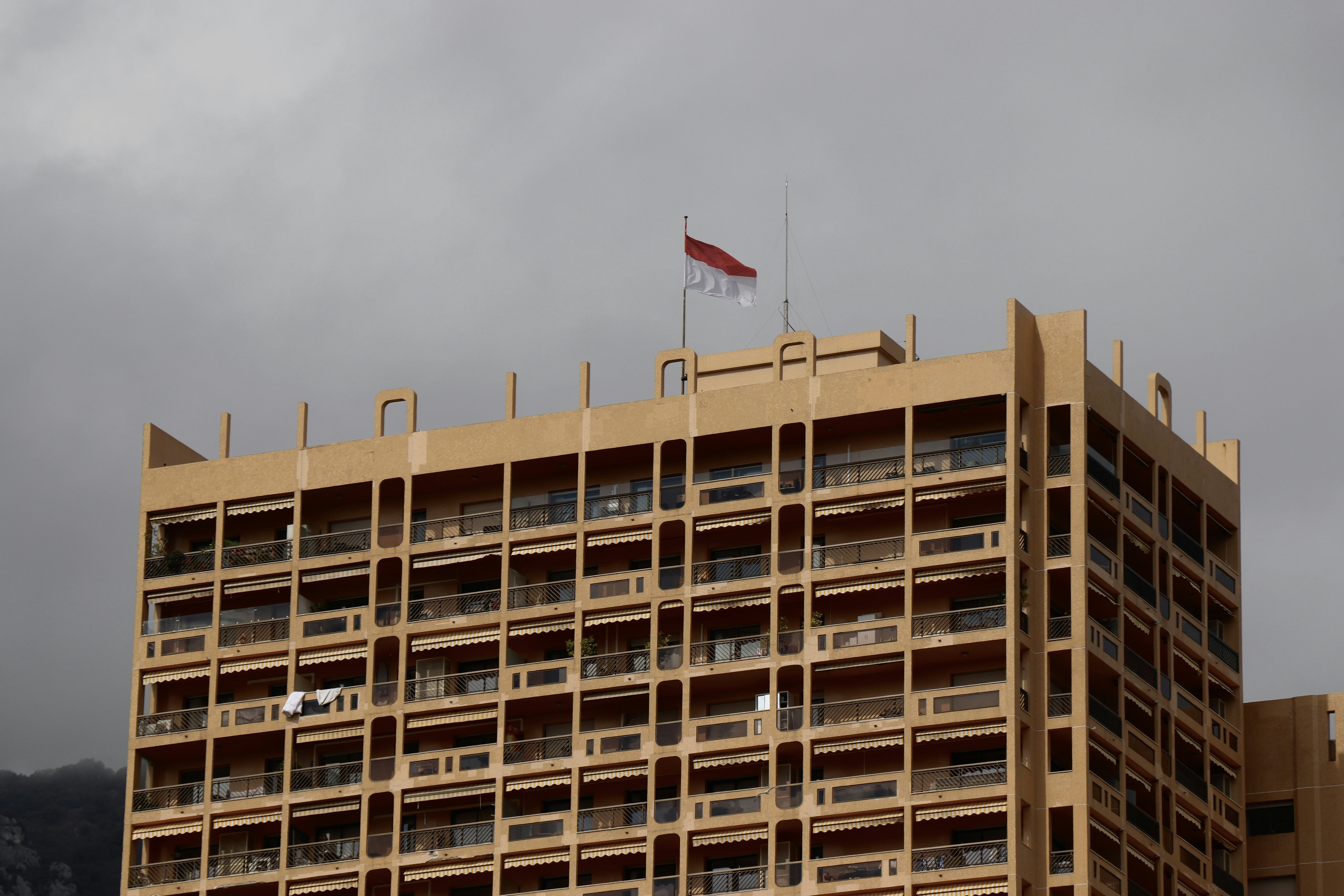 The Indonesian flag flying atop a tall tan apartment building under a cloudy grey sky
