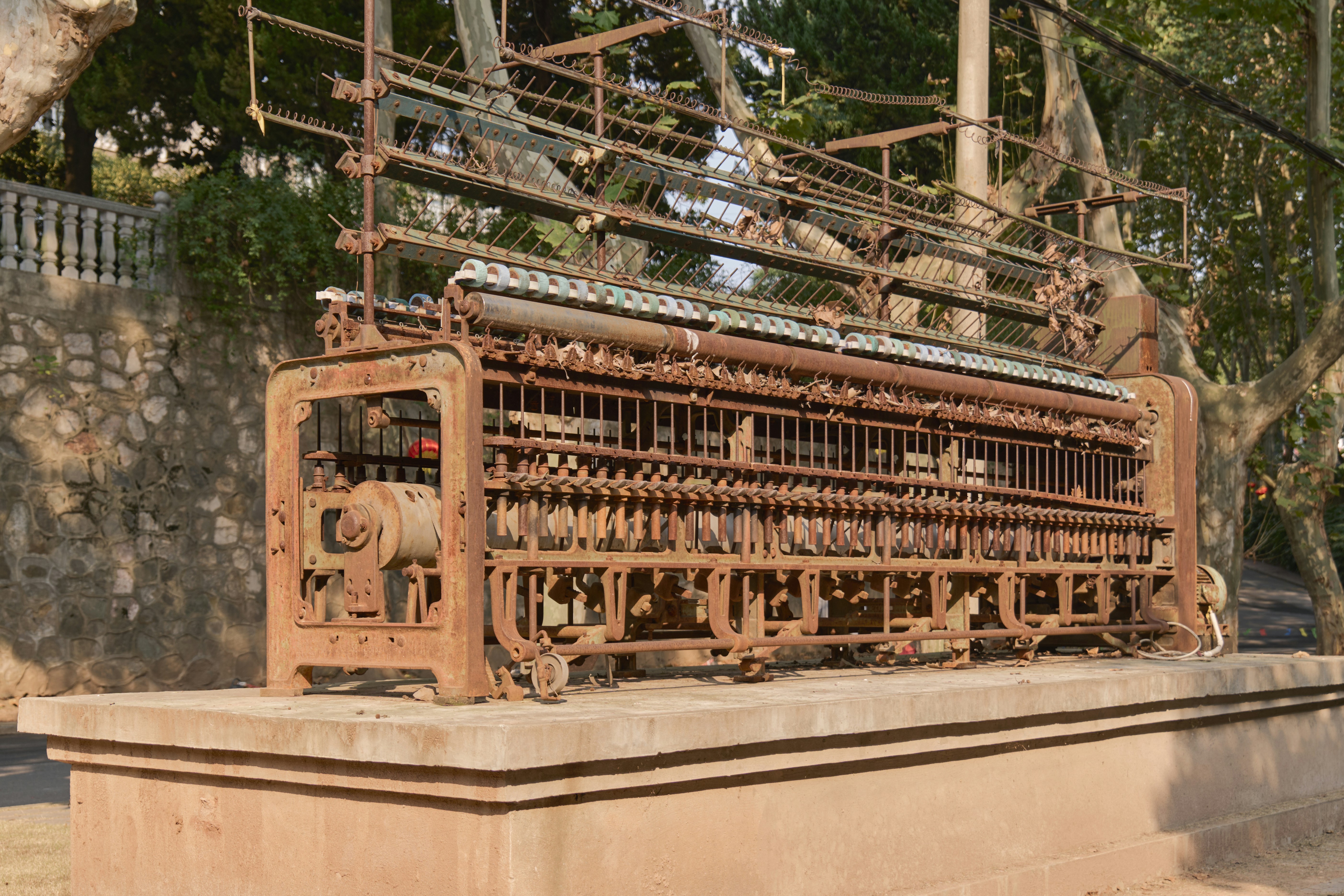 A rusted antique textile machine on a concrete pedestal in a park