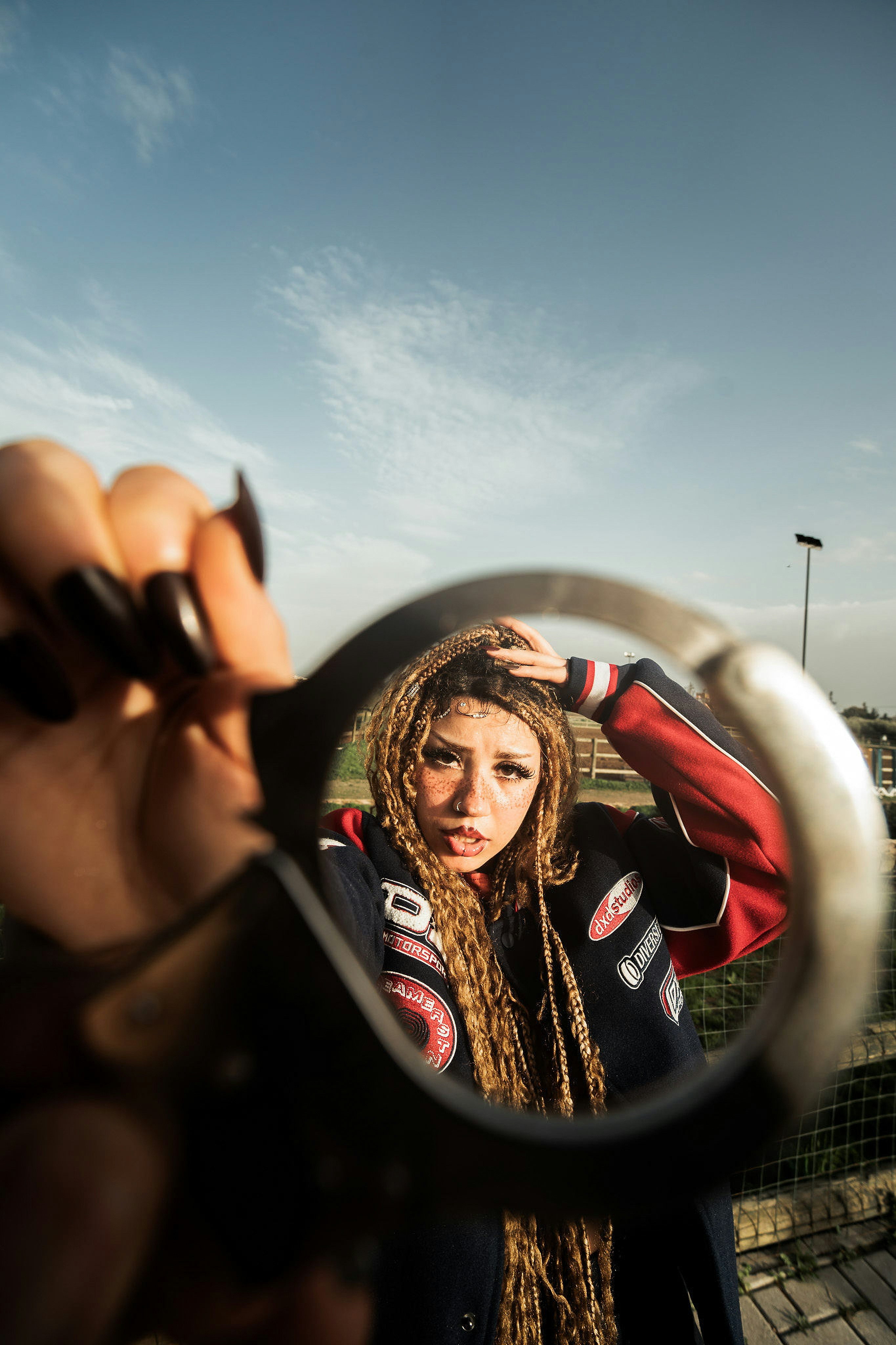 A person with braided hair and a varsity jacket seen through metal handcuffs outdoors