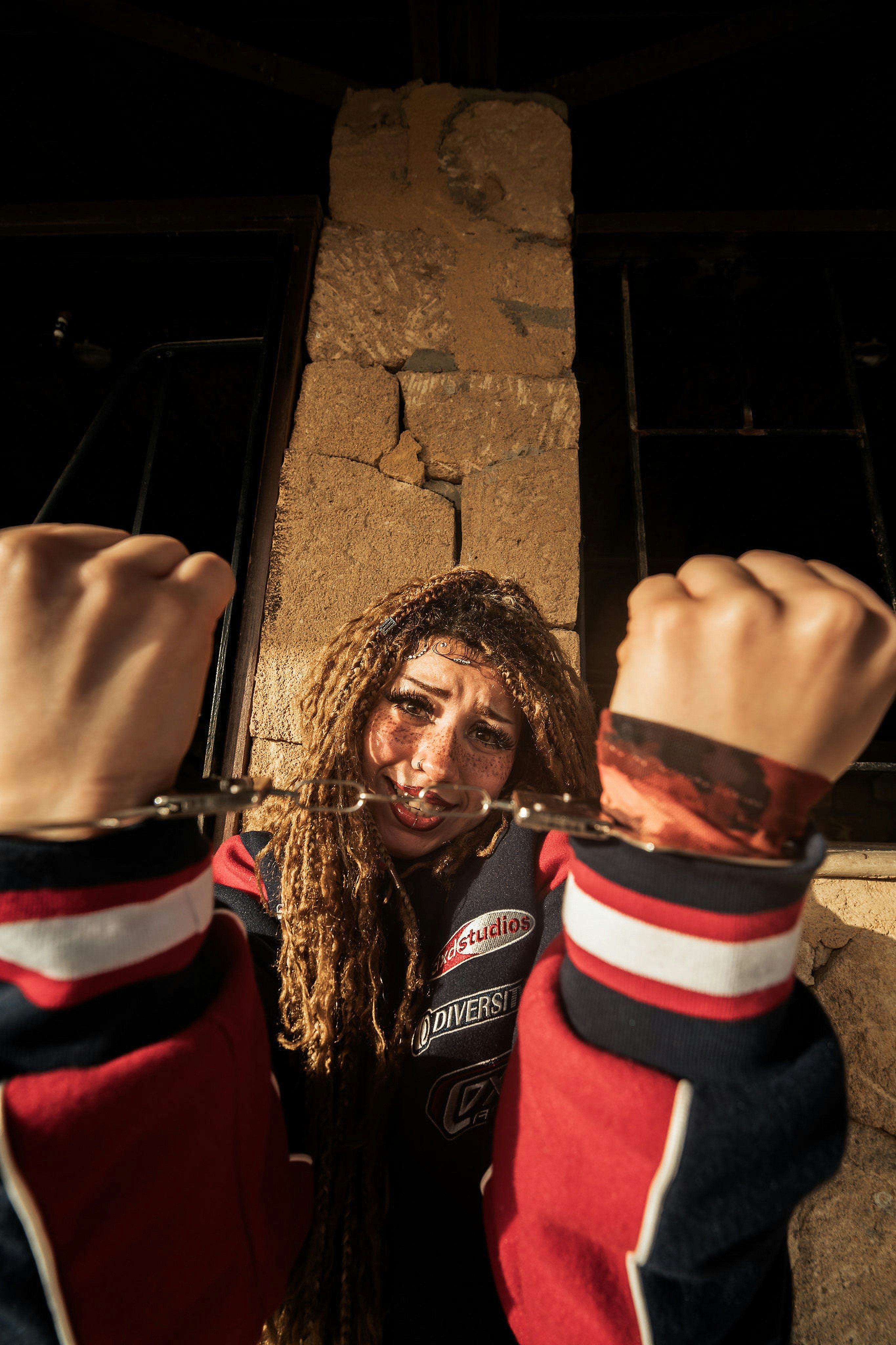 Una persona con i dreadlocks e le lentiggini che indossa le manette davanti a un muro di pietra