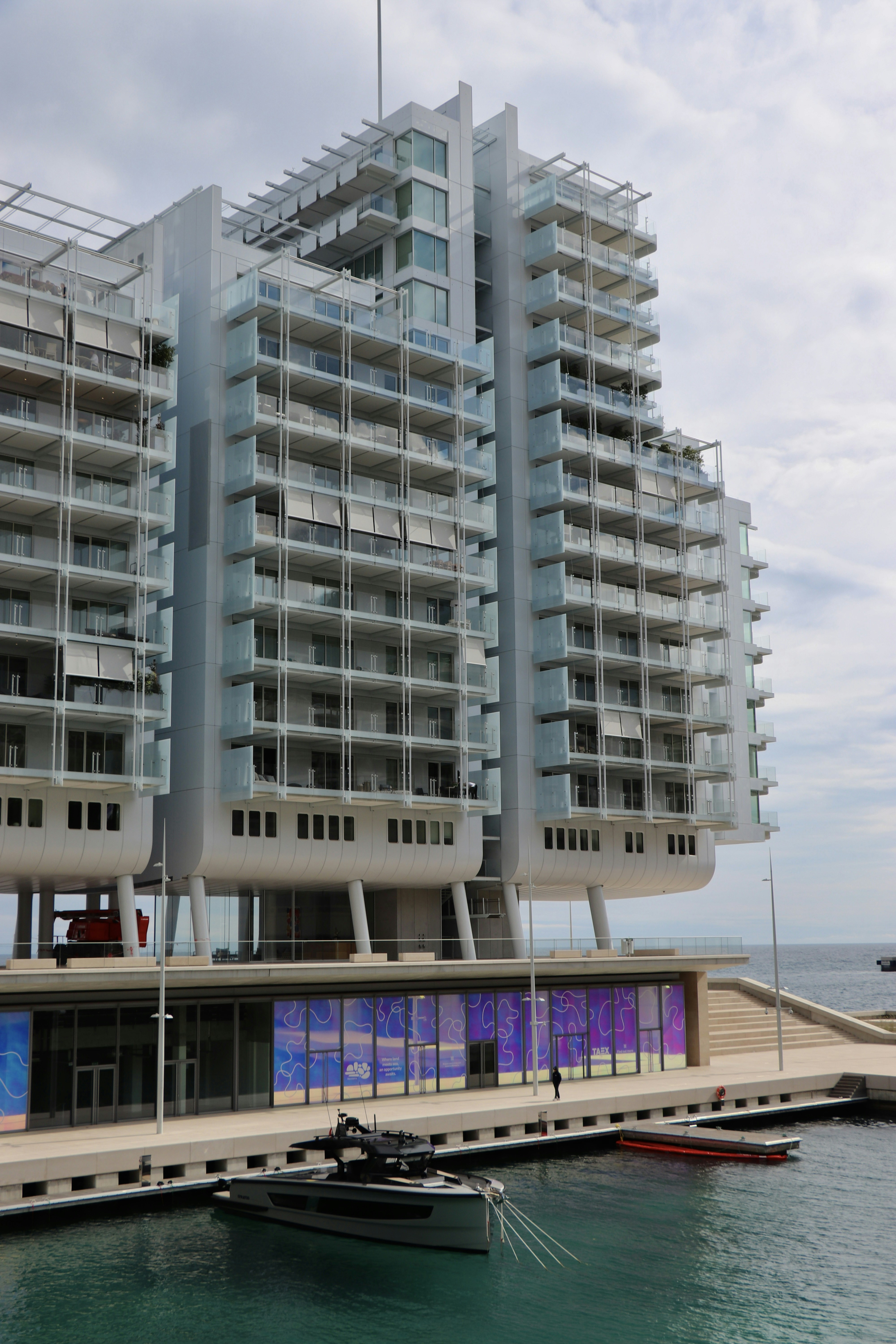 A modern high-rise apartment building with glass balconies overlooking a marina with a small boat
