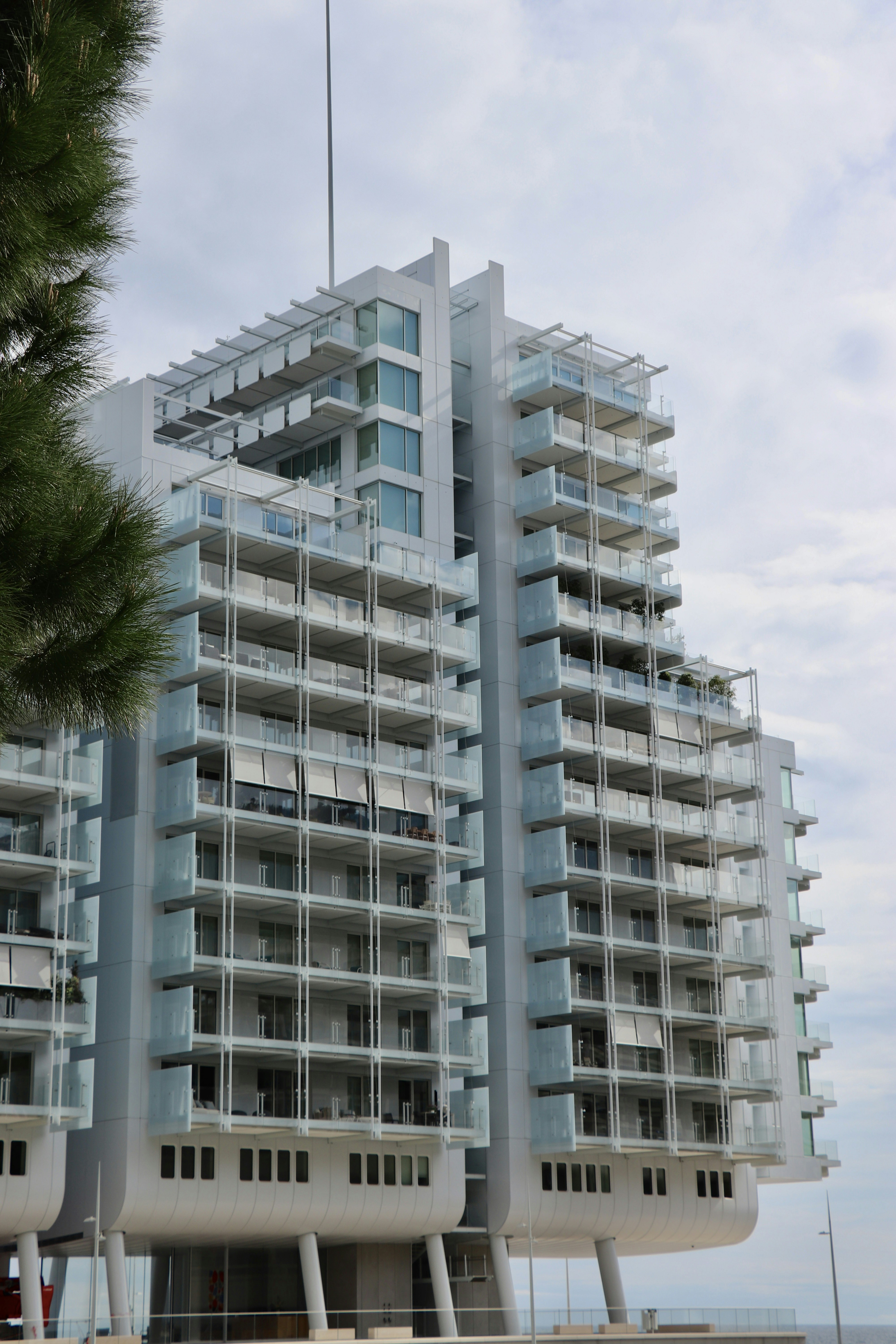A modern high-rise apartment building with glass balconies and white structural supports against a cloudy sky