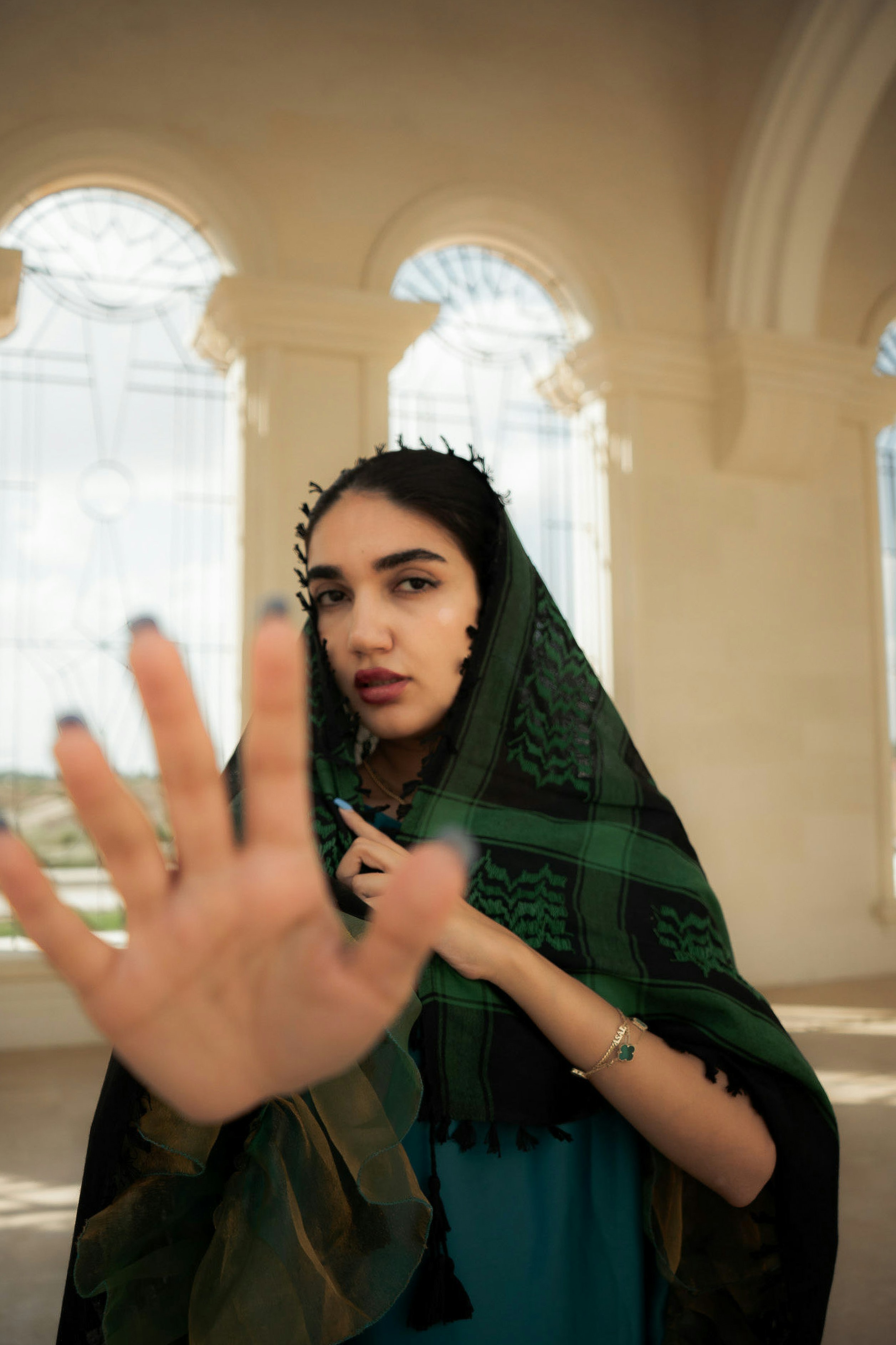A woman with a green and black patterned headscarf holding her hand out in a gesture
