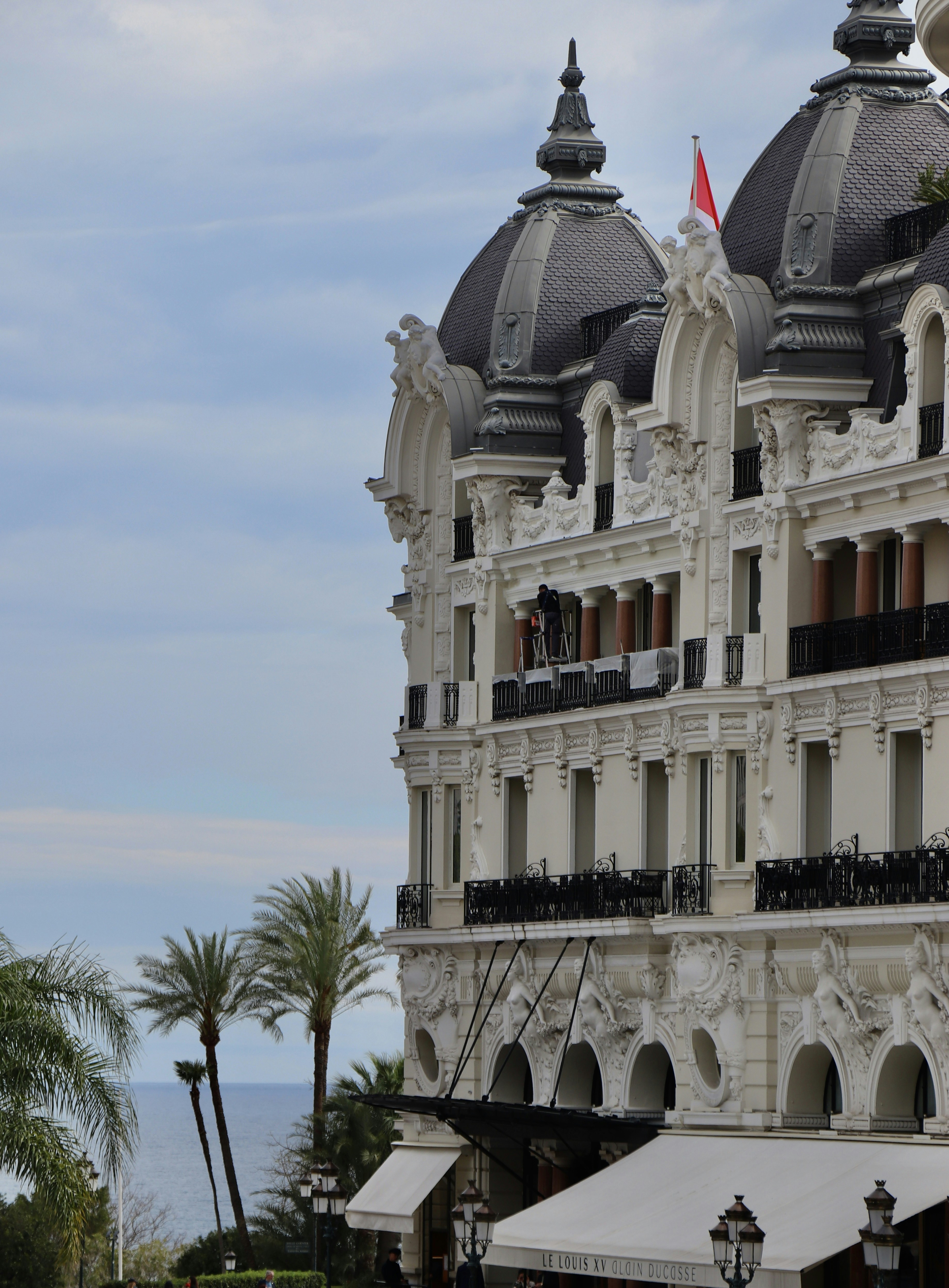 The ornate facade of the Hotel de Paris Monte-Carlo with palm trees and the Mediterranean Sea