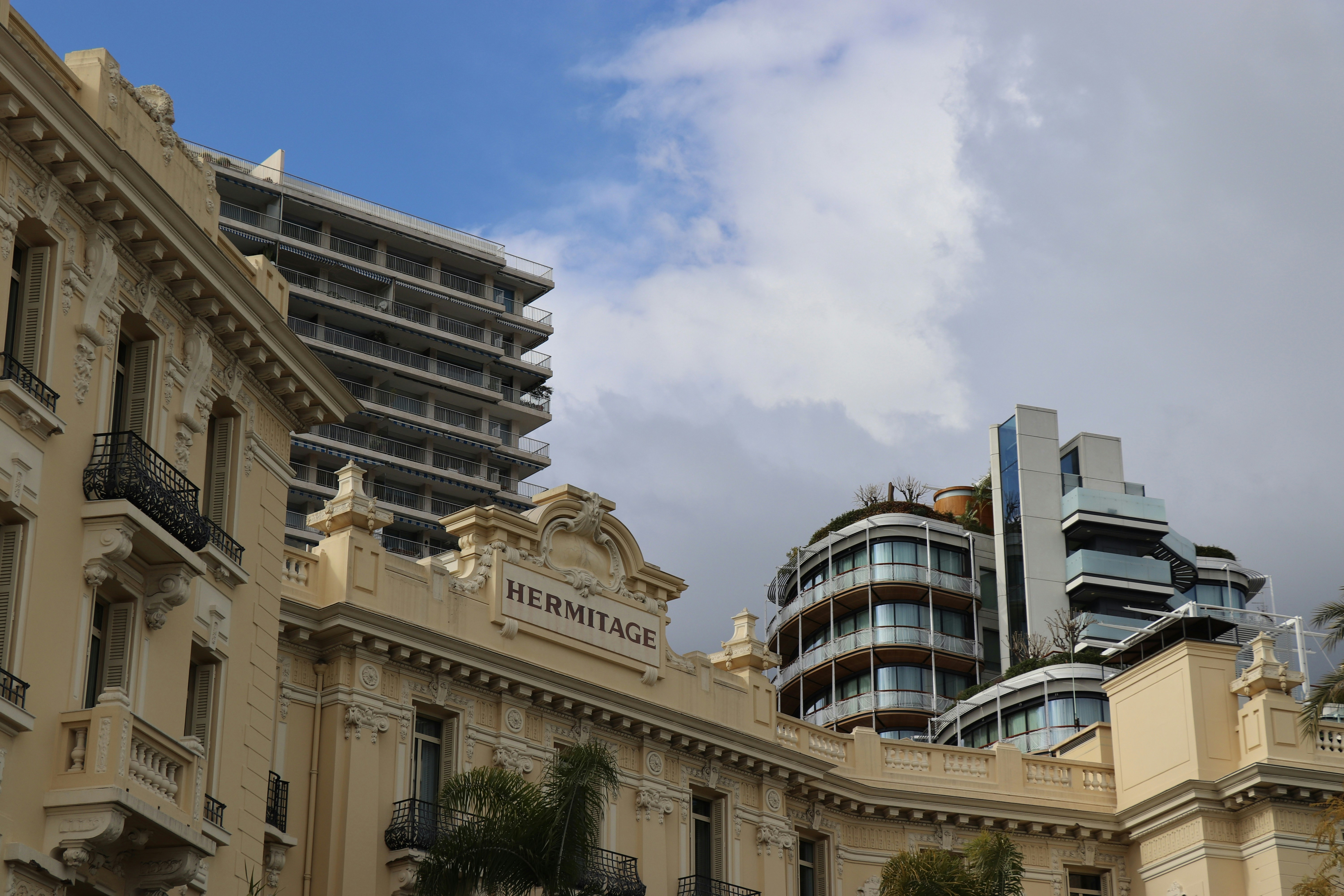 The Hotel Hermitage facade with ornate cream architecture below modern high-rise buildings in Monte Carlo